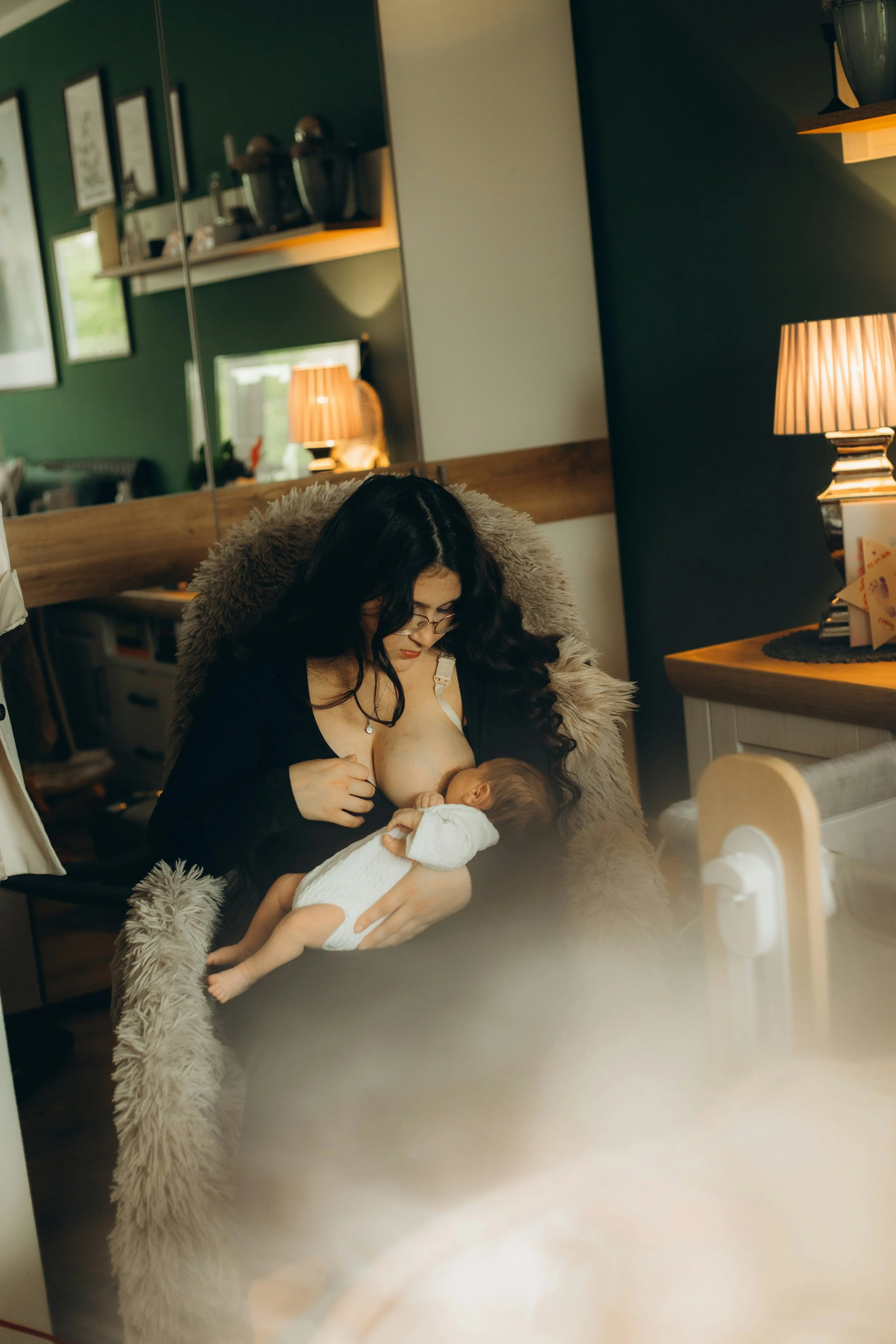 A parents breastfeeding a baby in a comfortable chair at home