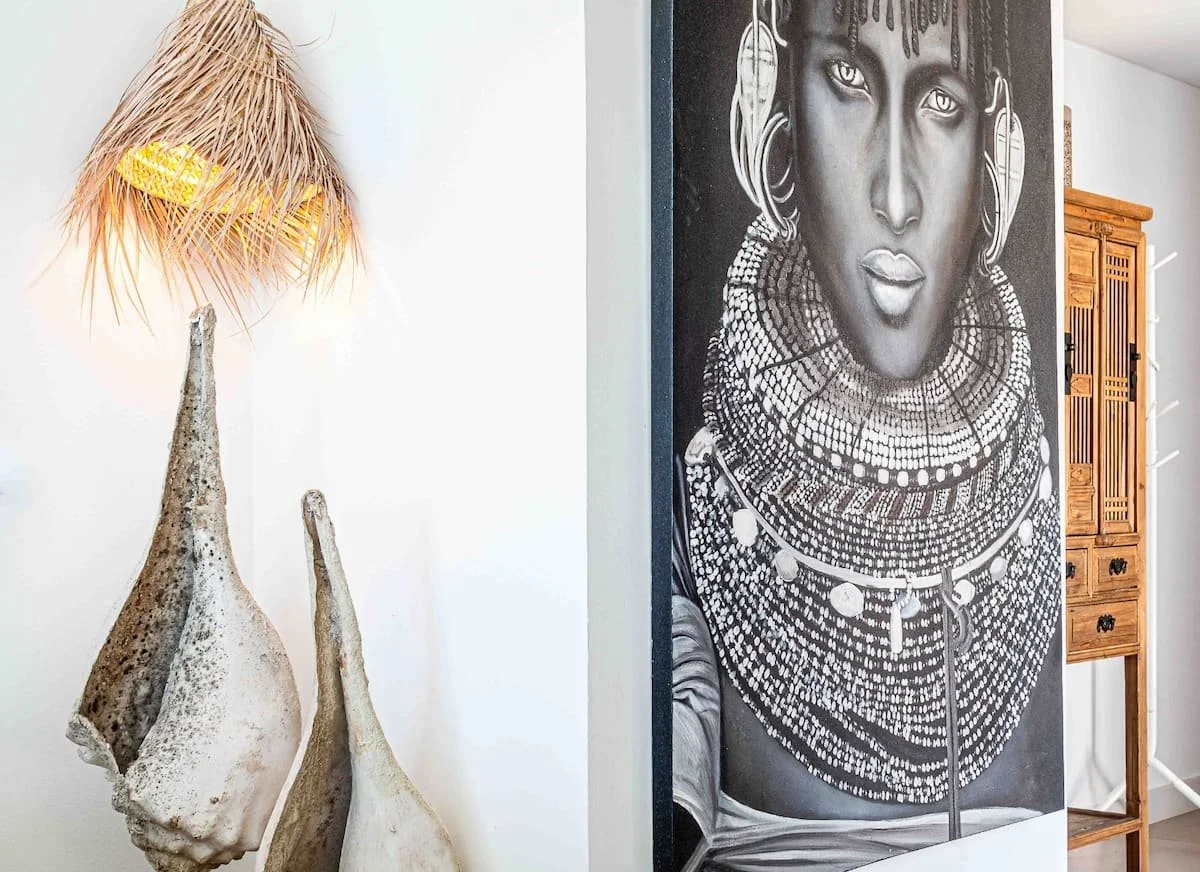 Decoración interior con una lámpara de juncos, dos huesos grandes y una pintura en blanco y negro de un retrato de una mujer con accesorios tribales.