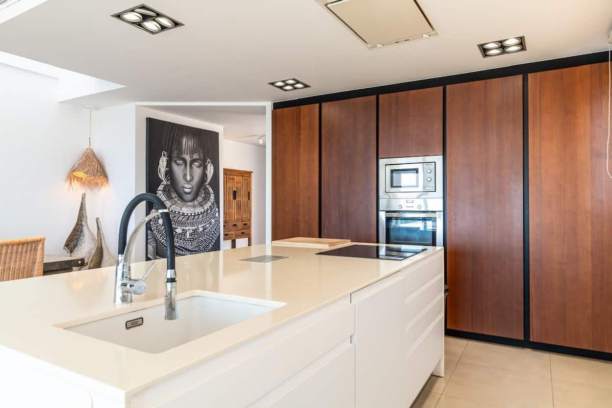 Cocina moderna con isla, fregadero, horno y microondas empotrados, armarios de madera y decoración artística en la pared.