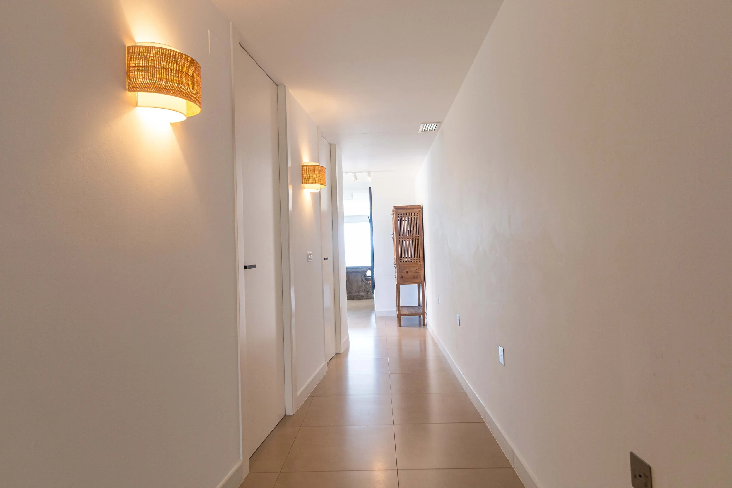 Un pasillo en una casa moderna con paredes blancas, pared decorativa, una lámpara de pared y un armario de madera del lado derecho.
