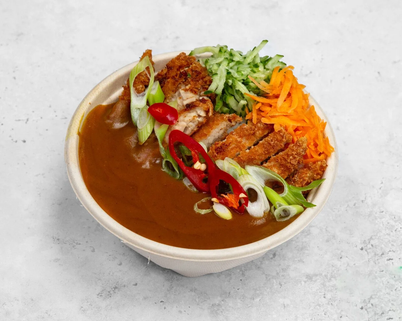 Bowl of Japanese Chicken Katsu curry with sliced fried chicken, shredded carrots, chopped green onions, shredded cucumber, and sliced red chili peppers.