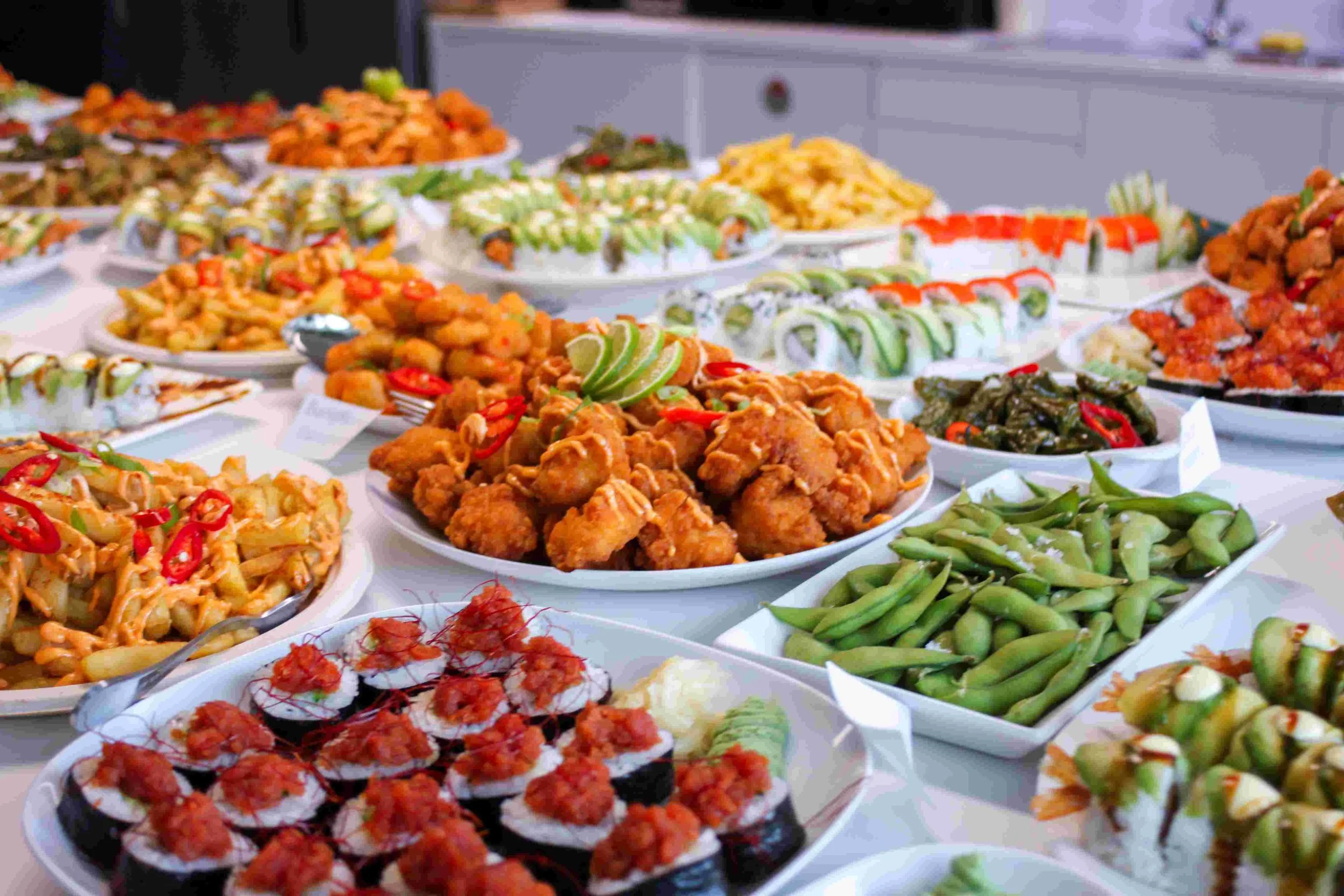 A table filled with various Asian dishes, including fried chicken, sushi rolls, green beans, and other colorful appetisers.