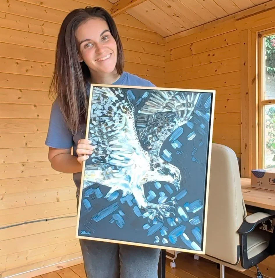A woman smiling and holding a framed artwork of an osprey in flight.
