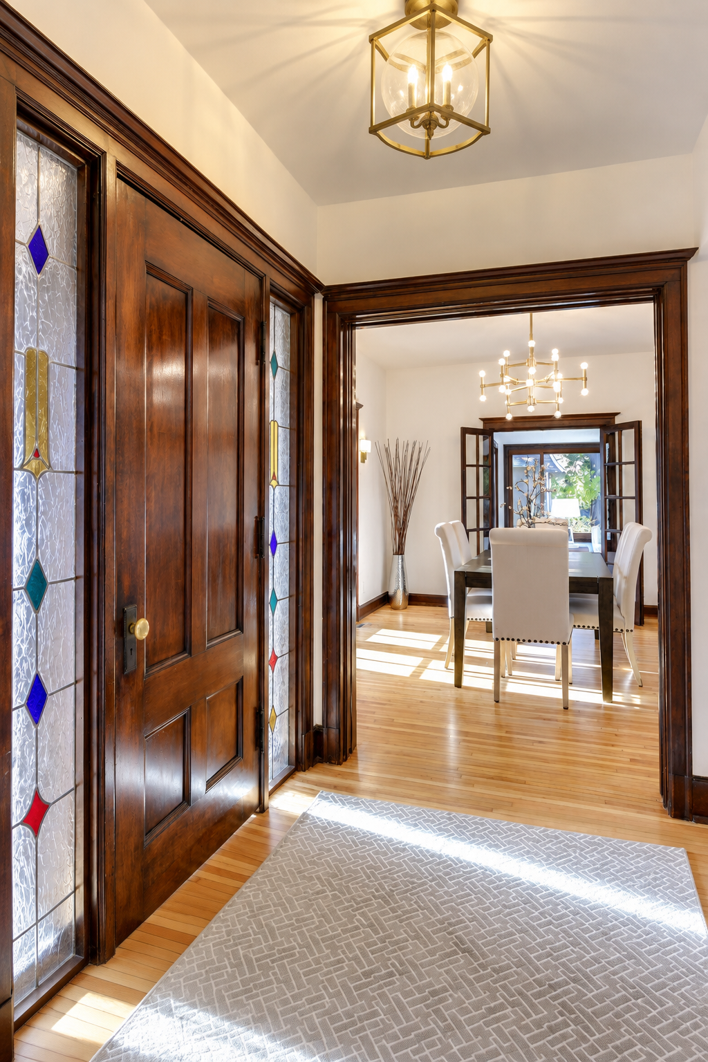 View from the entryway into a dining room with hardwood floors, dark wood trim, a chandelier, and white upholstered chairs around a dark wood table.