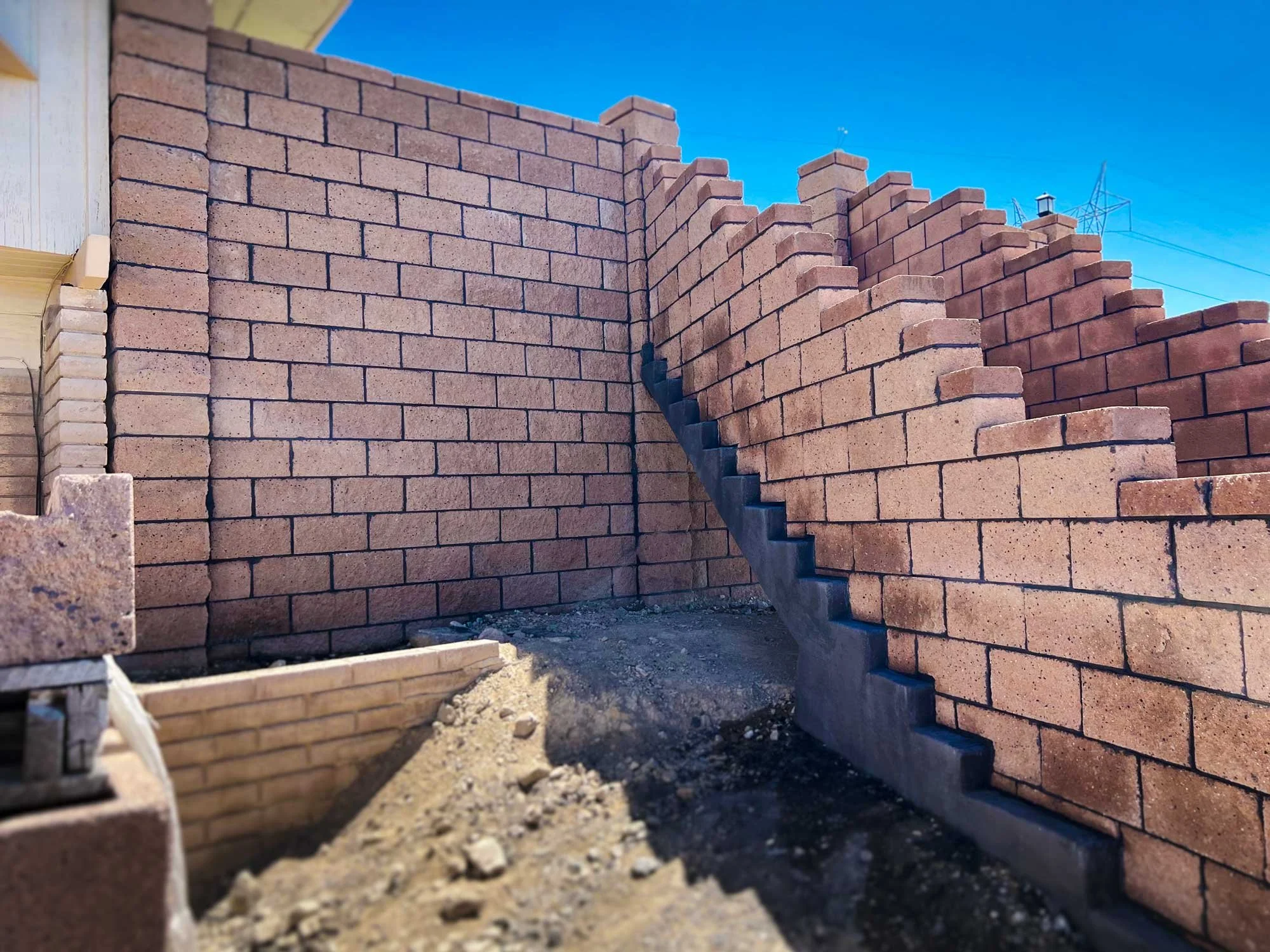 Brick wall under construction with a staircase built into it, blue sky in the background, and a light fixture on top of the wall.