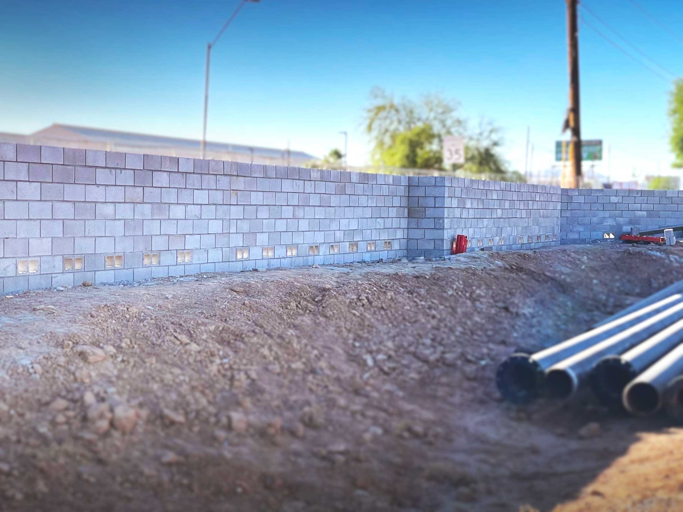 Construction site with a brick wall, gravel ground, and construction tools, under a clear blue sky.