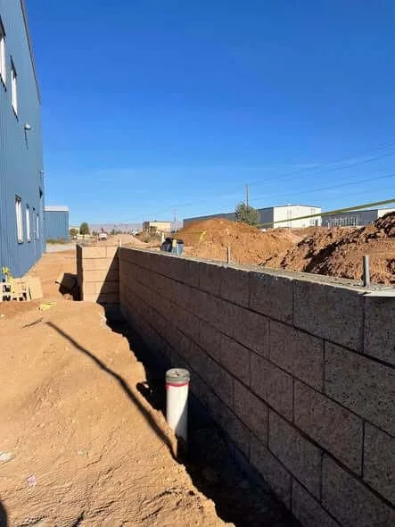 Construction site with a newly built concrete block wall, dirt, and construction materials under a clear blue sky.