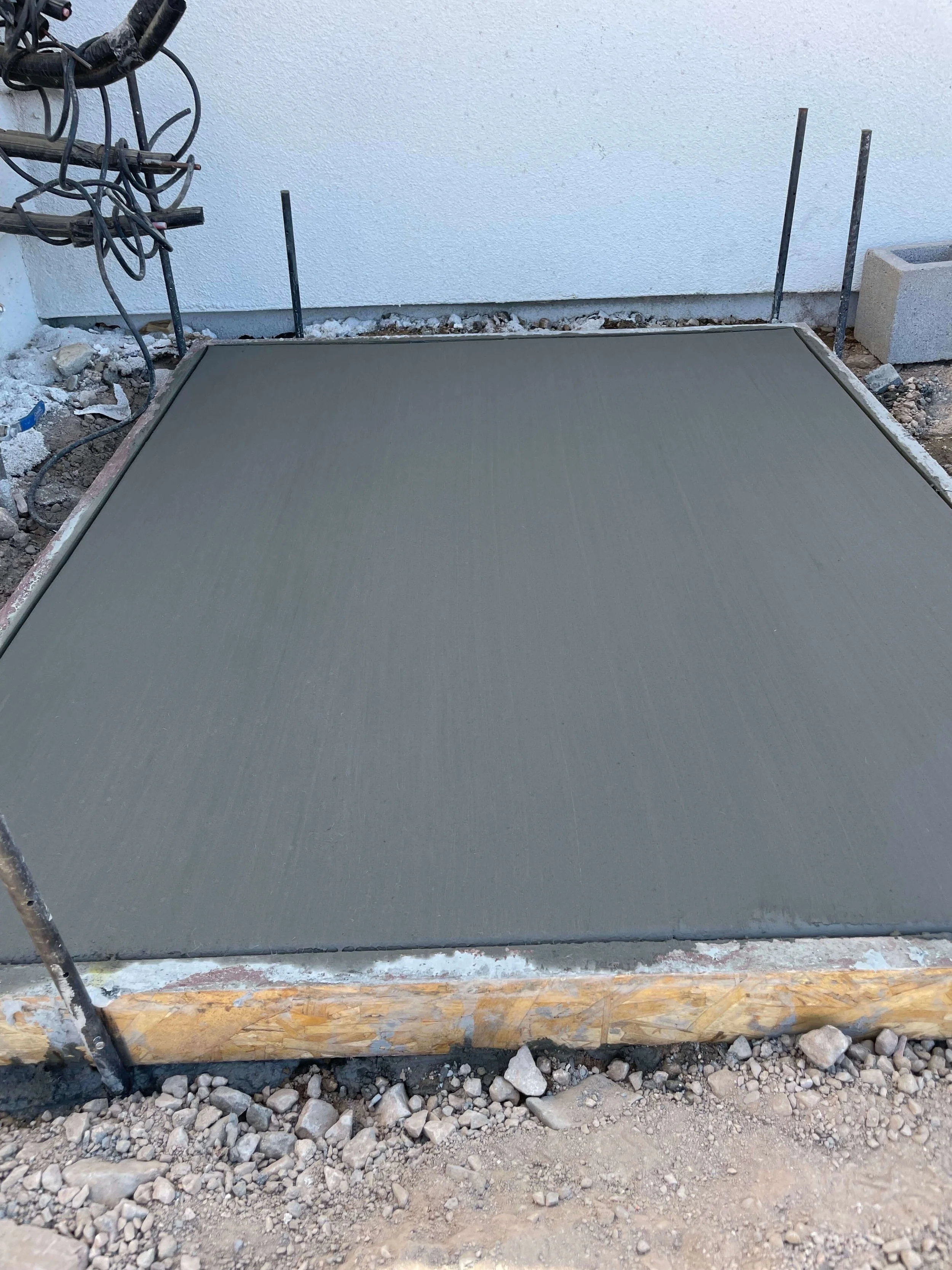 Freshly poured concrete slab on a construction site, with construction braces and gravel around it.