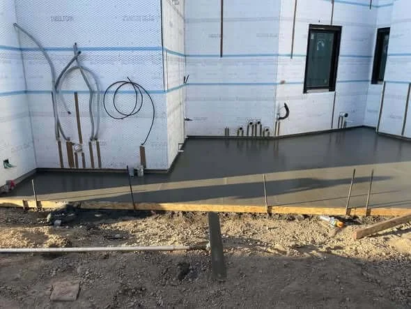 Construction site of a building with a freshly poured concrete foundation, unfinished exterior walls, and exposed wiring.