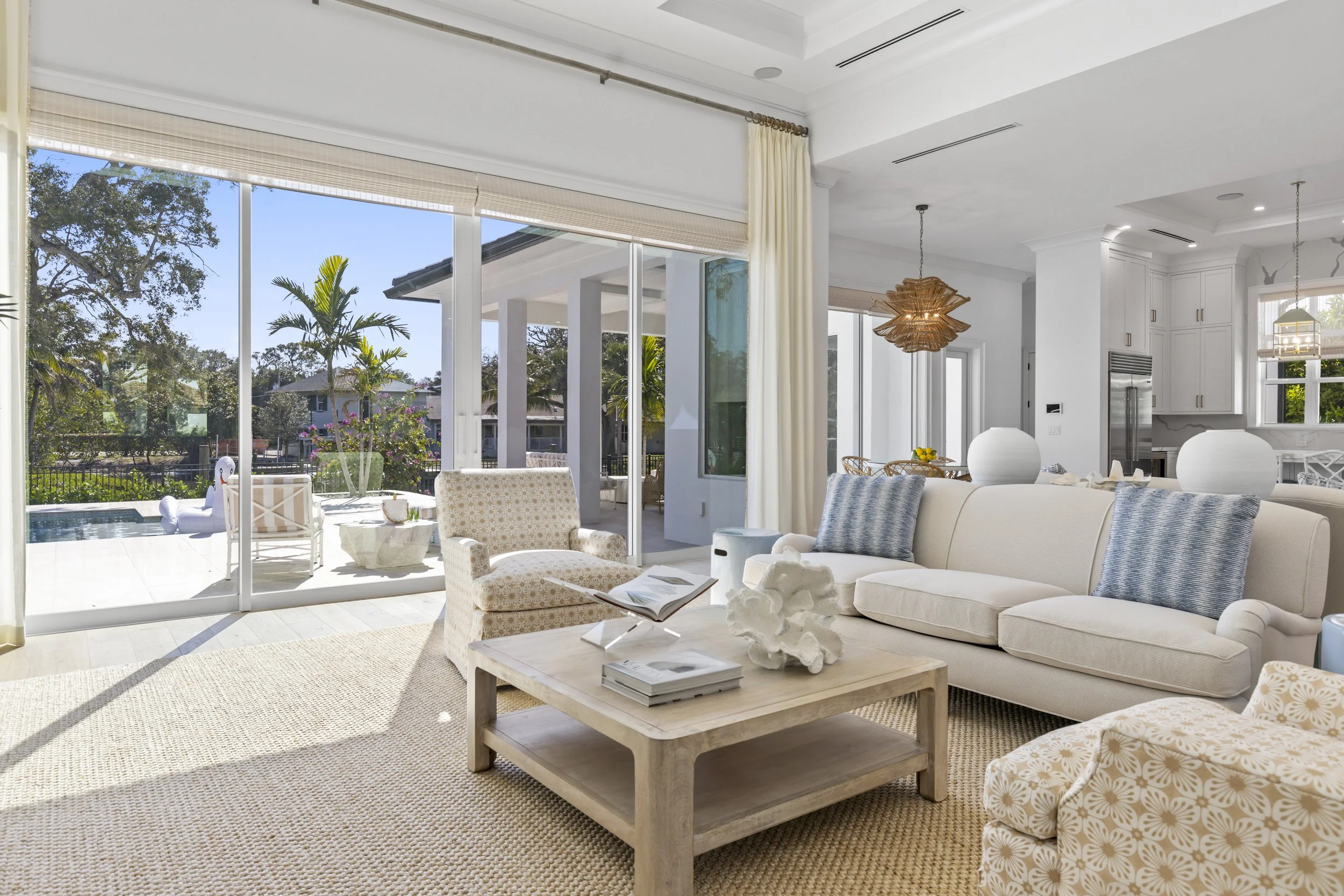 Bright living room with large glass sliding doors opening to a backyard with trees and plants, including a pool and outdoor seating.