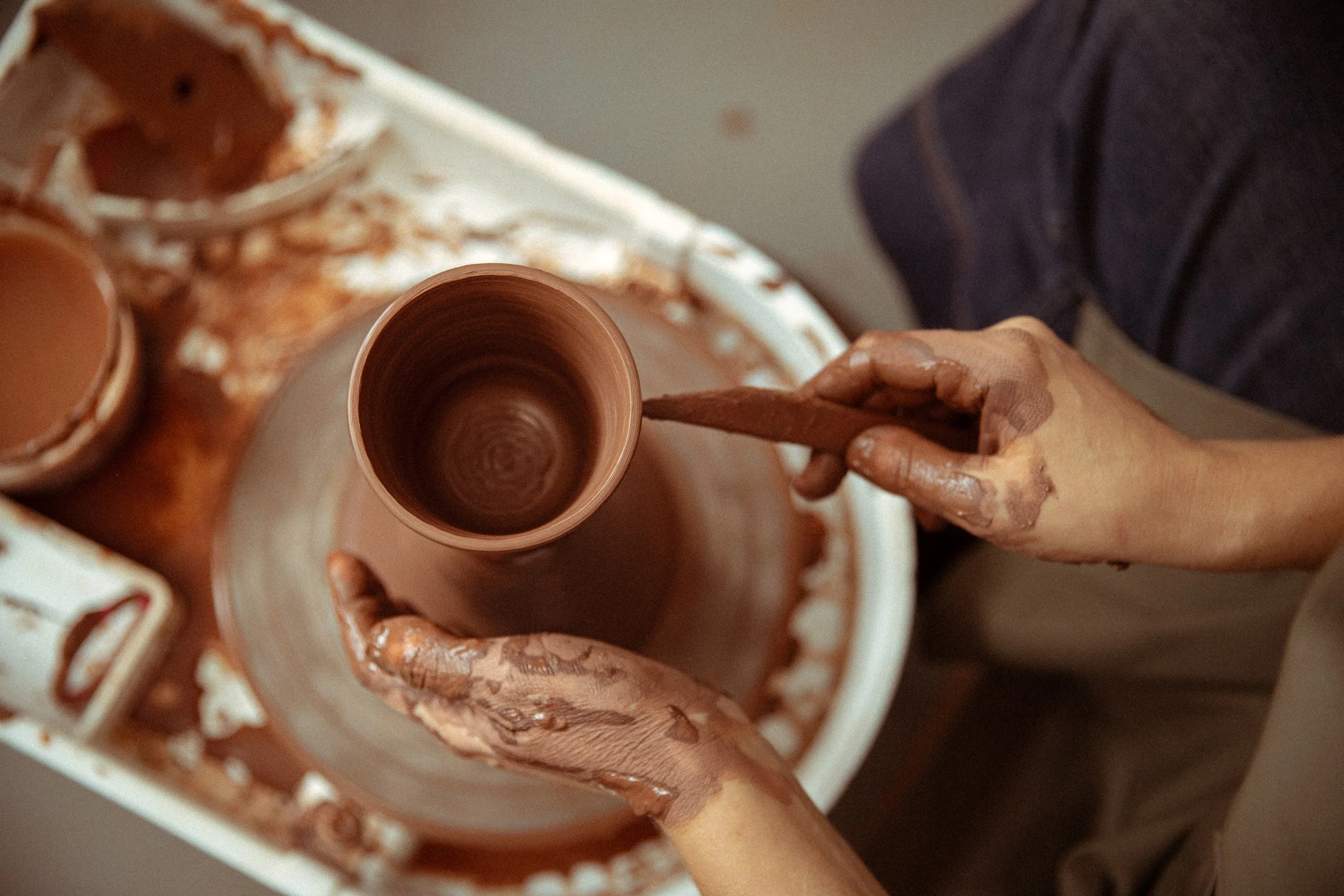Person shaping a clay pottery piece on a pottery wheel.