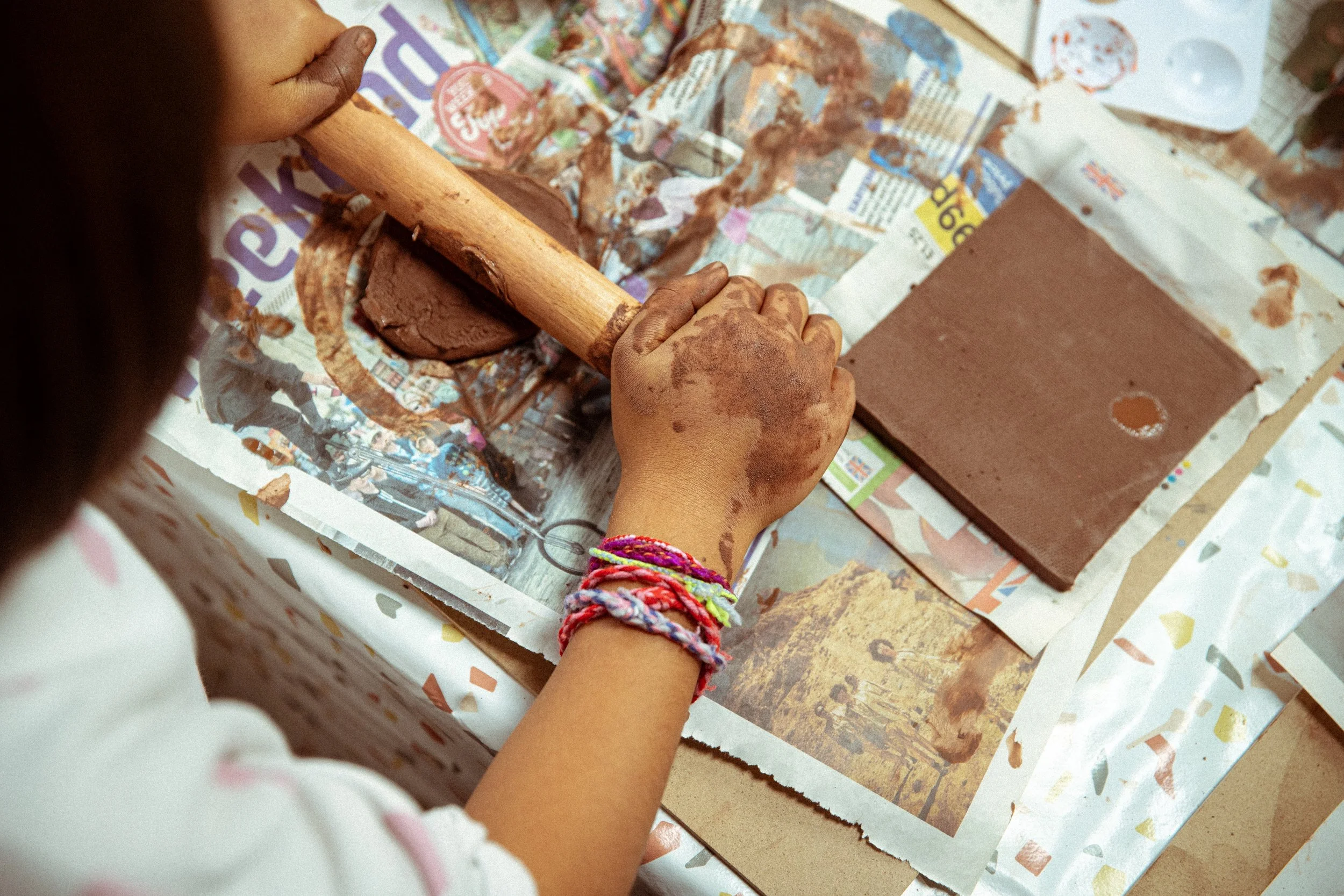 A person using a wooden mallet to shape clay on newspaper-covered surface.