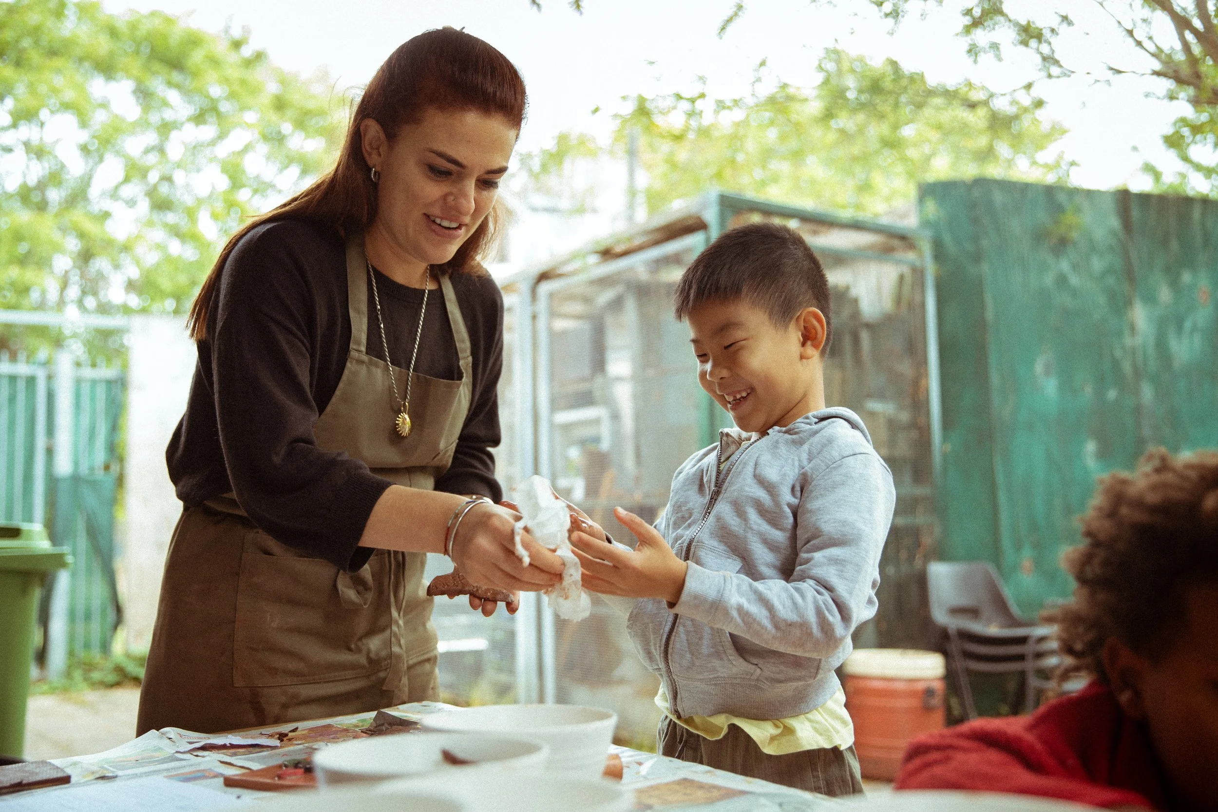 A woman and a young boy smiling and playing with cotton candy outdoors.