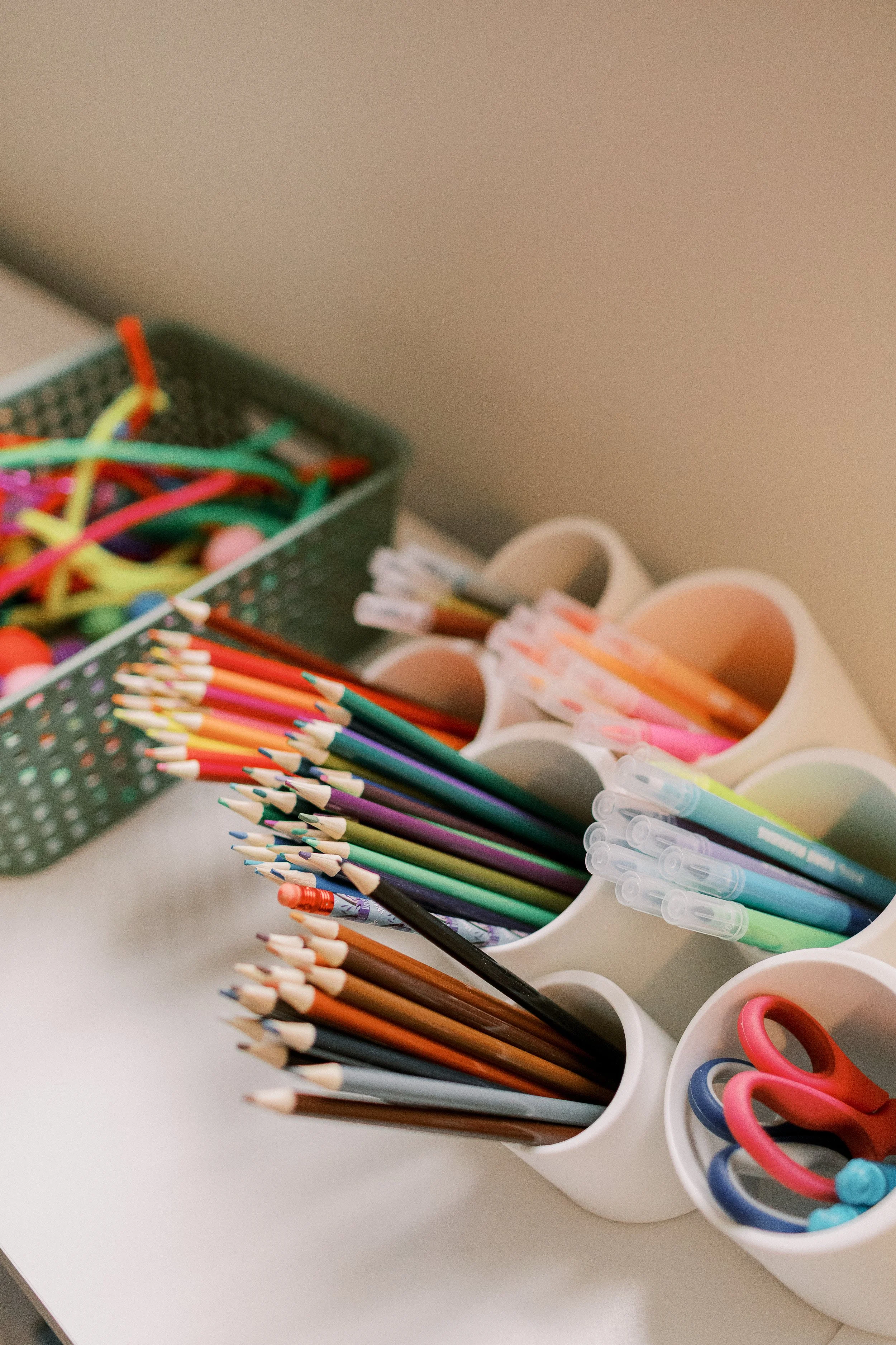 A collection of colorful pens, pencils, and scissors organized in white containers on a white surface.