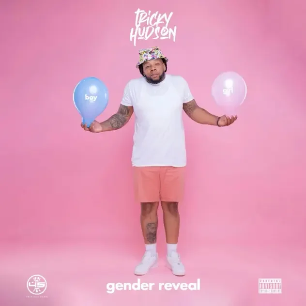 Tricky Hudson standing against a pink background holding blue and pink balloons for a gender reveal