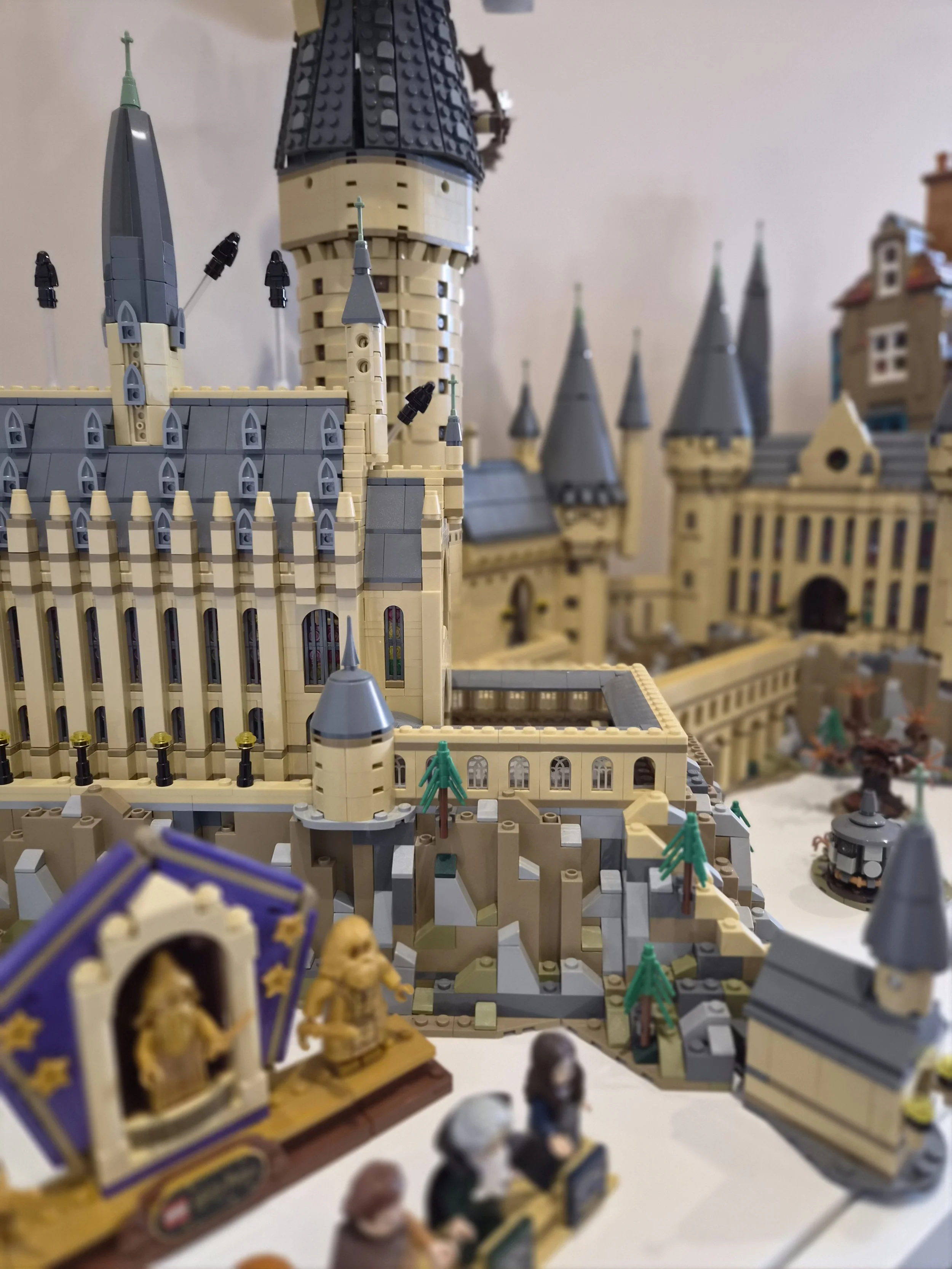 A detailed LEGO model of a castle with towers, spires, and walls, featuring various small decorative elements and miniature figures in the foreground.