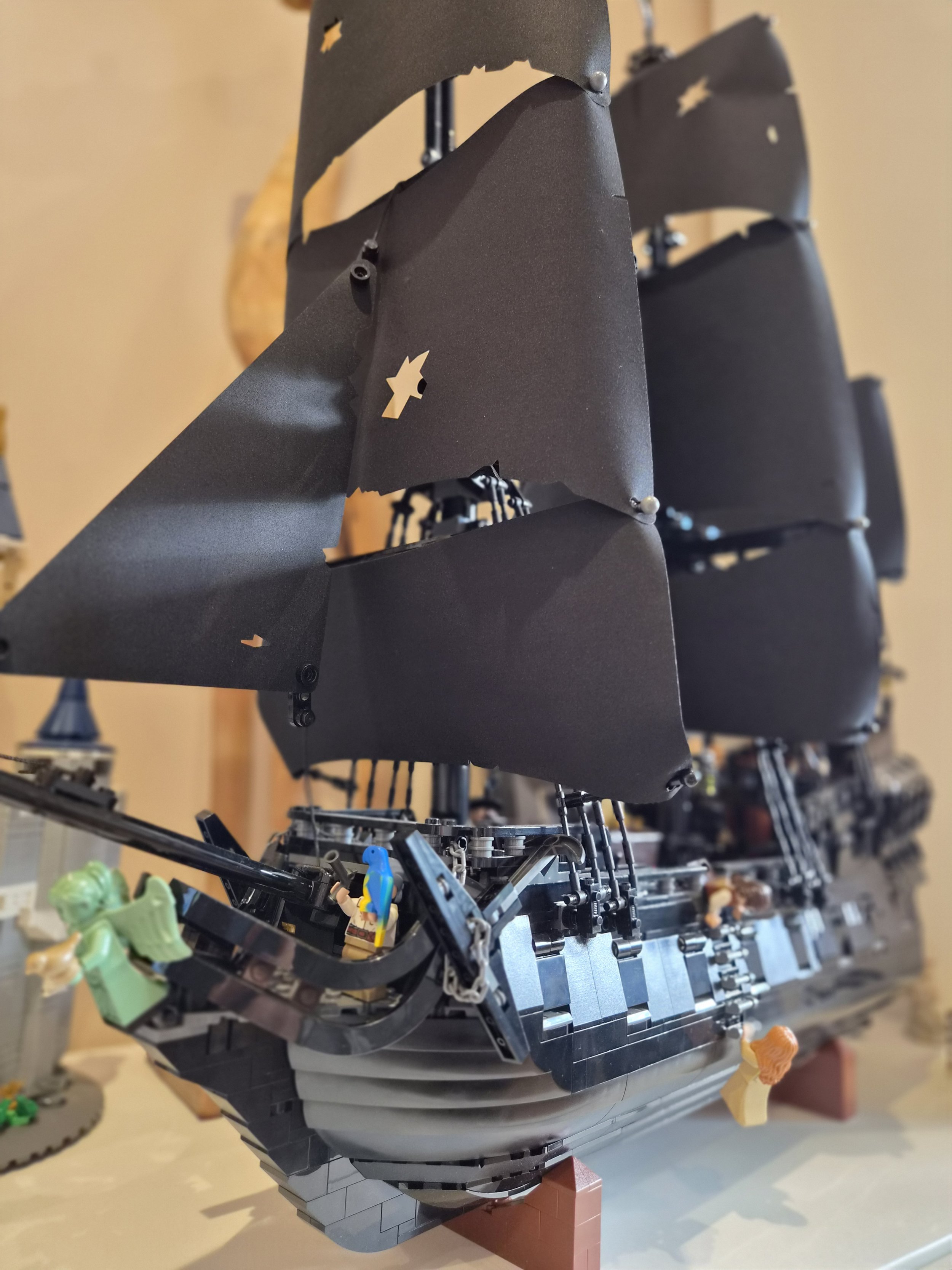 Lego pirate ship with Pirate minifigures on deck, black sails with yellow stickers, and mini animals, displayed on a table.