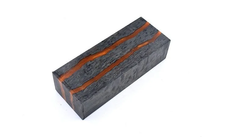 A rectangular block of stabilized curly birch wood with a black and gray colored surface, featuring two parallel orange-red resin streaks running along its length.