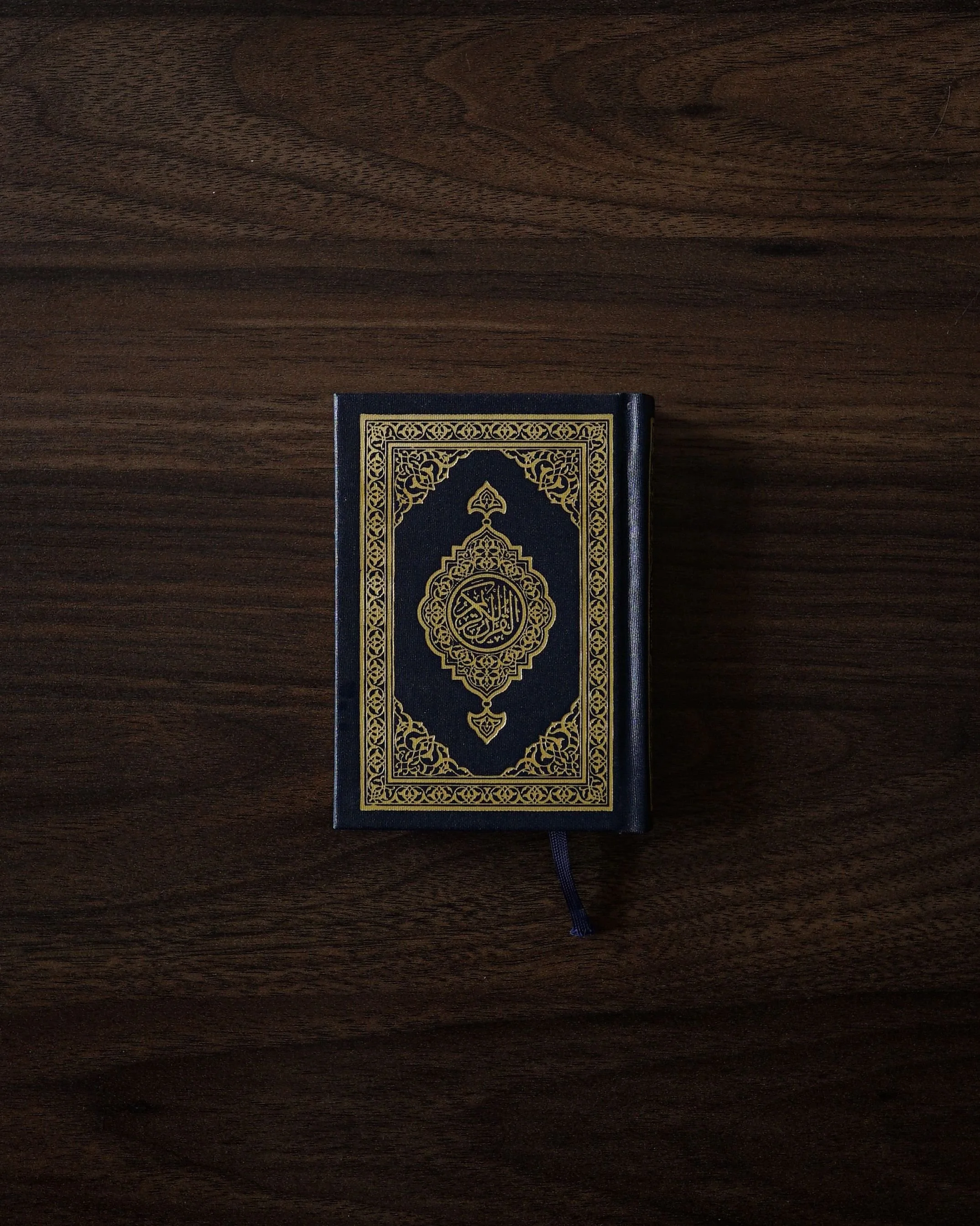 A closed black Bible with gold intricate design on the cover, lying on a dark wooden surface.