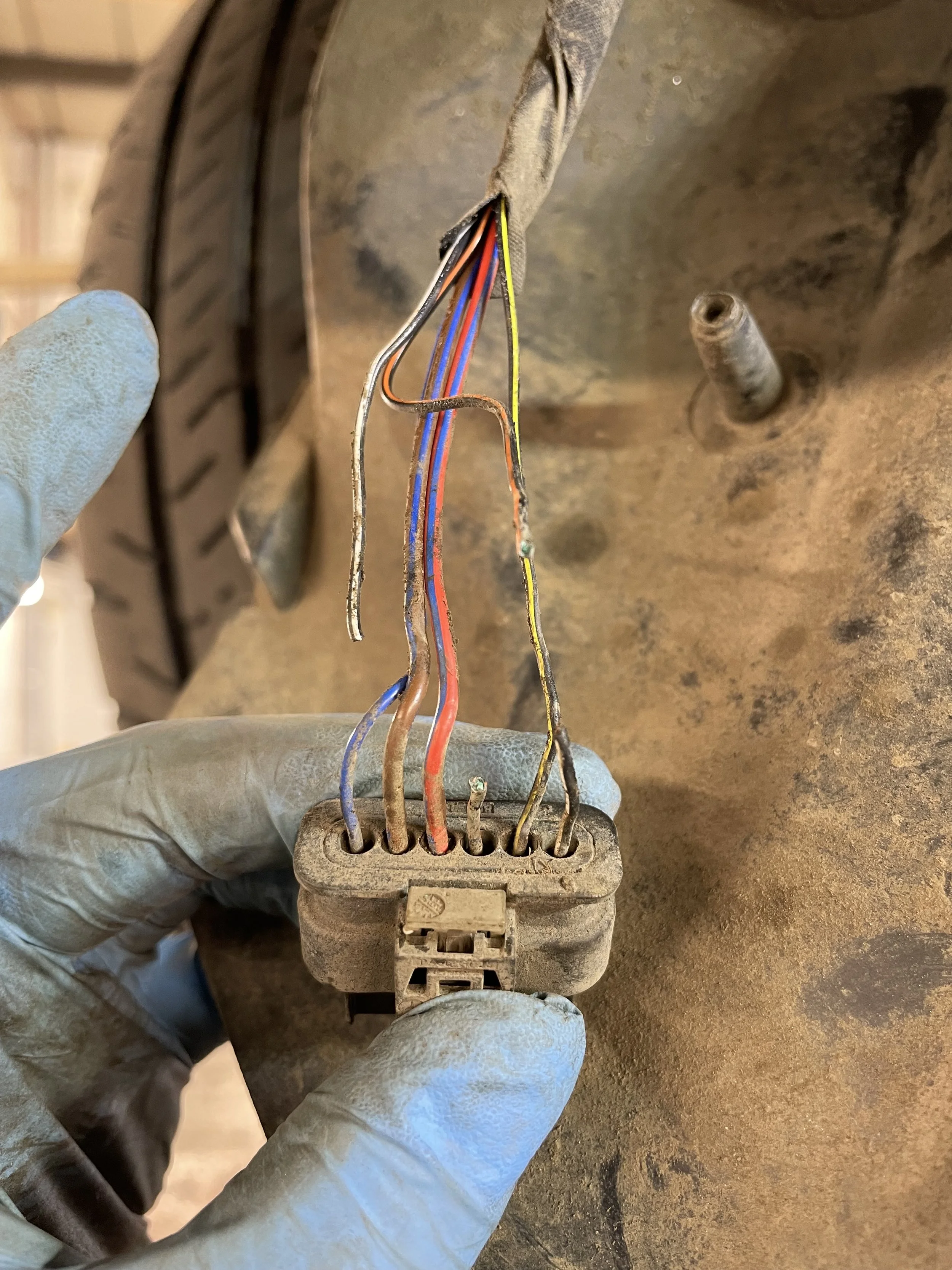 A person's hand wearing a blue glove holding an old, dusty electrical connector with several frayed and exposed wires of various colors.