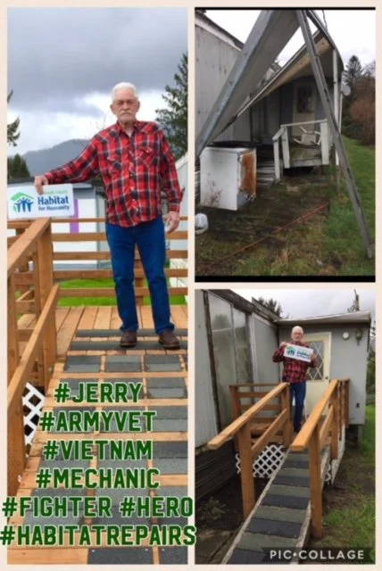 A man standing on a newly built wooden porch, holding a Habitat for Humanity sign; in the background, a damaged house with a boarded-up window and construction materials, indicating a home renovation project.