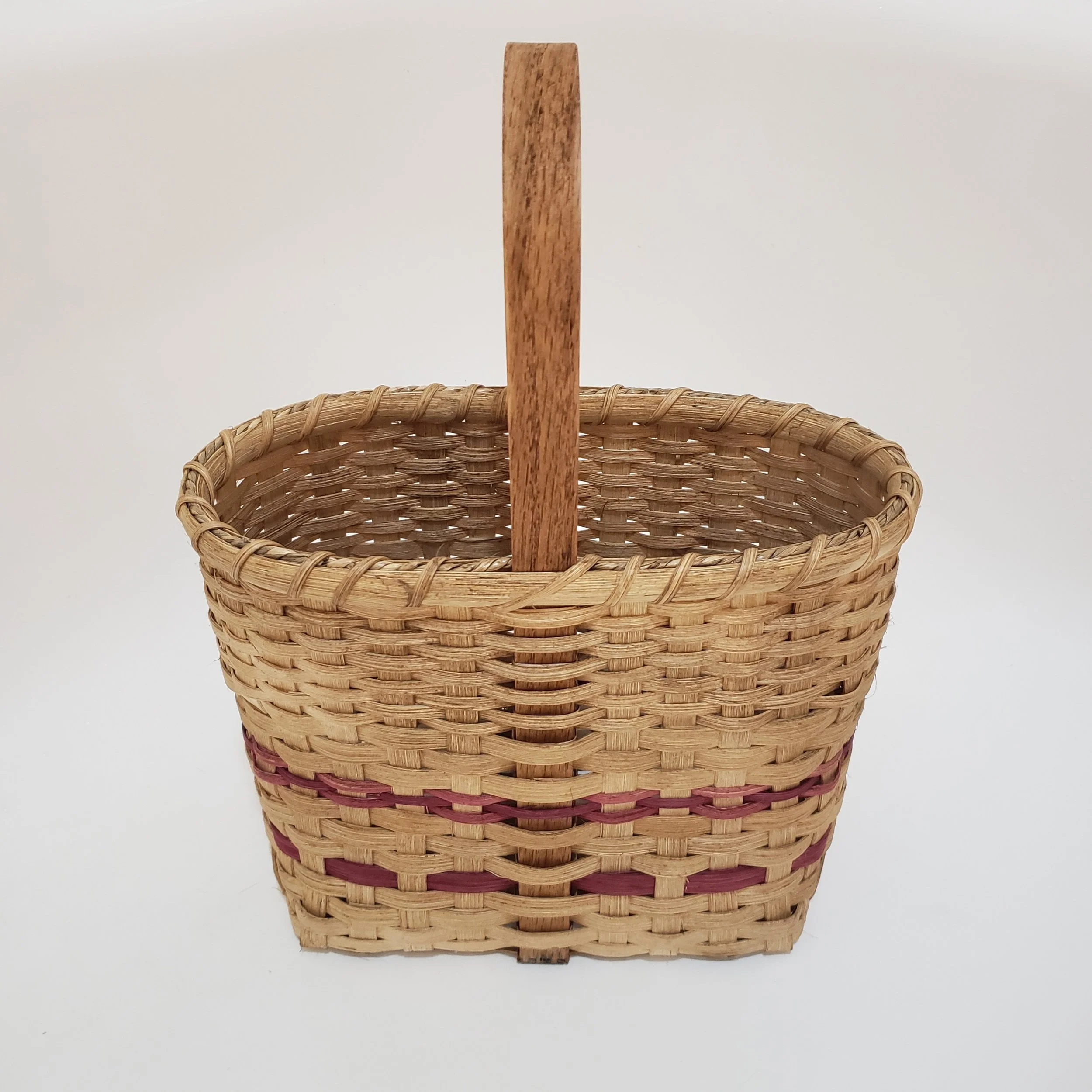 A woven wicker basket with a natural color, featuring a tall wooden handle, set against a plain white background.