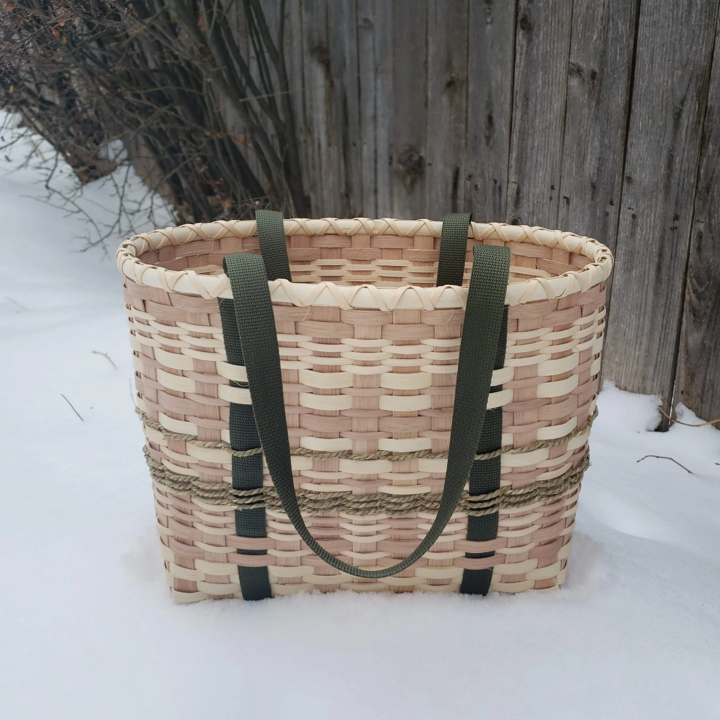 Basket hanging on a snow-covered wooden fence in a winter outdoor setting.