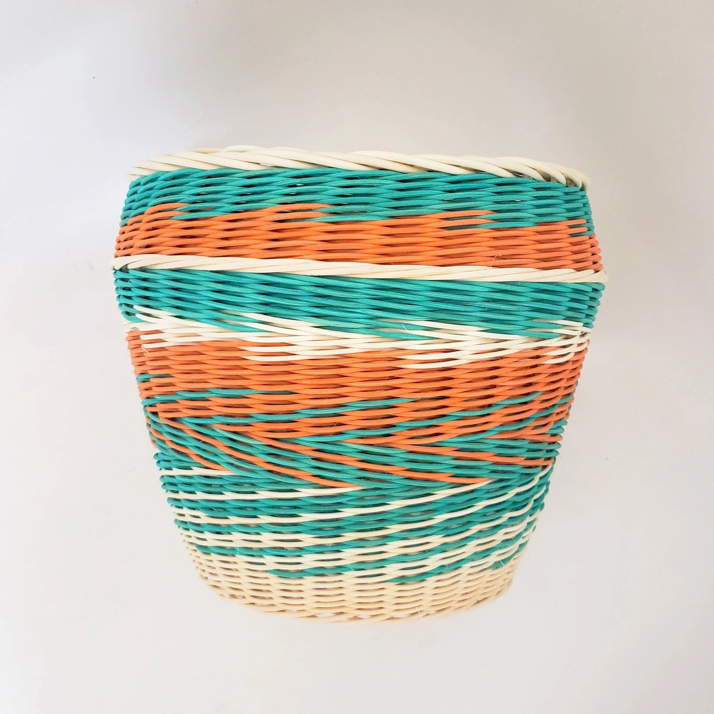 Colorful woven basket with white, turquoise, orange, and beige horizontal stripes, empty, against a white background.