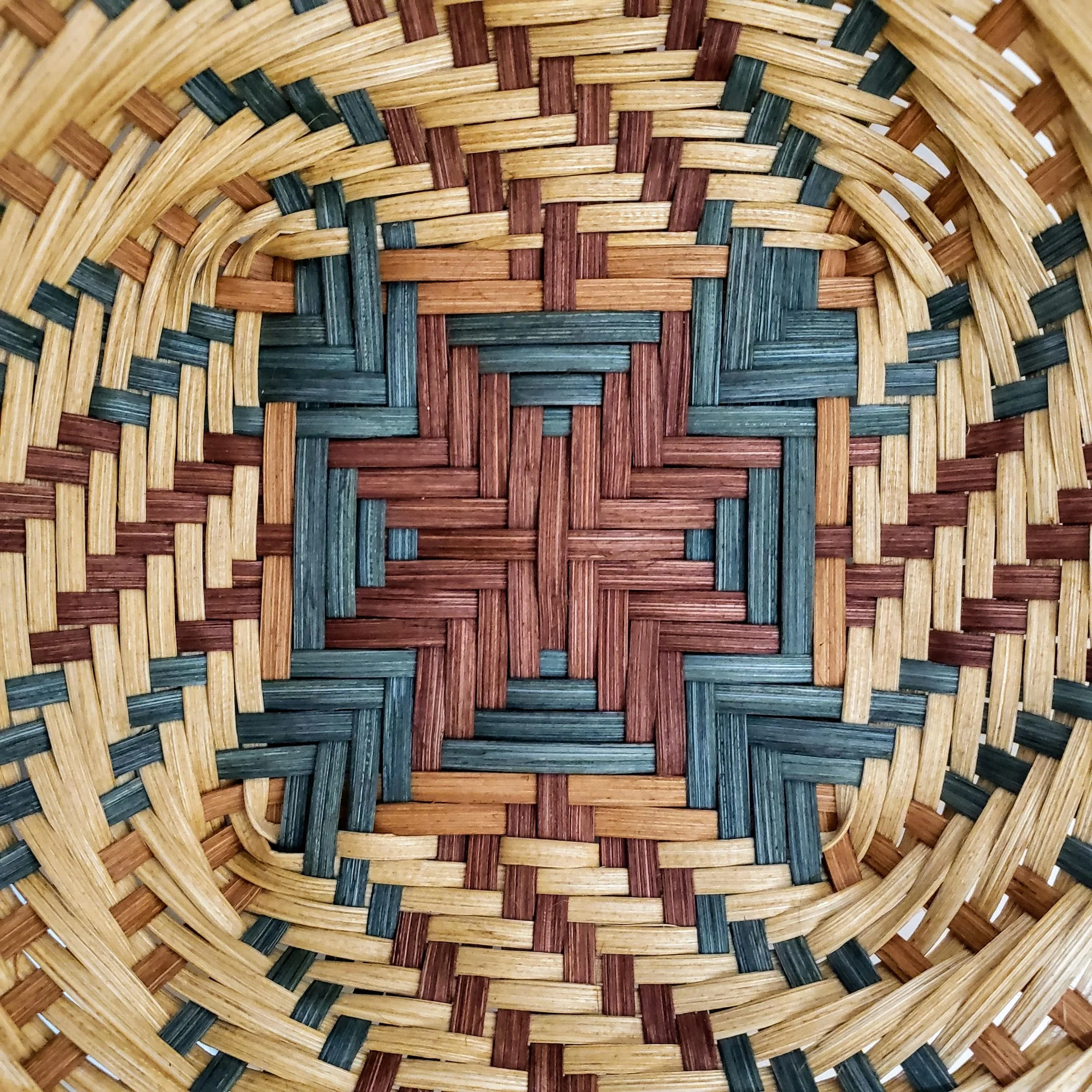 Close-up of woven wicker basket showing intricate pattern and natural brown, tan, red, and dark green colors.