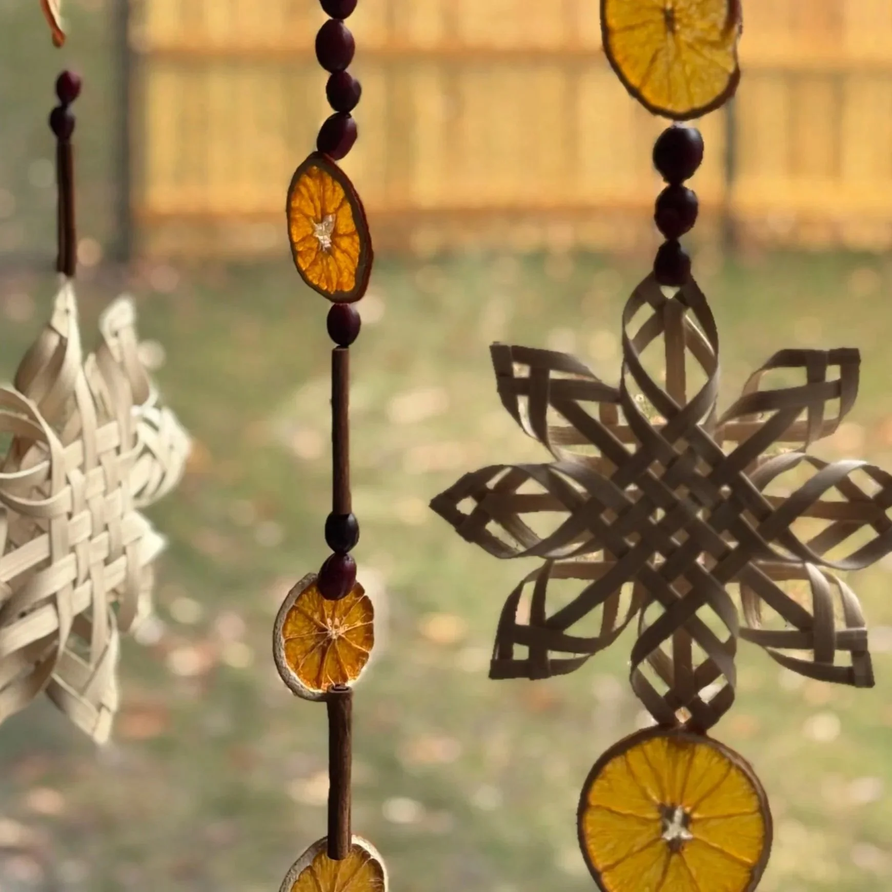 Close-up of decorative hanging ornament made of dried orange slices and dark beads, reflected on a glass or mirror surface.