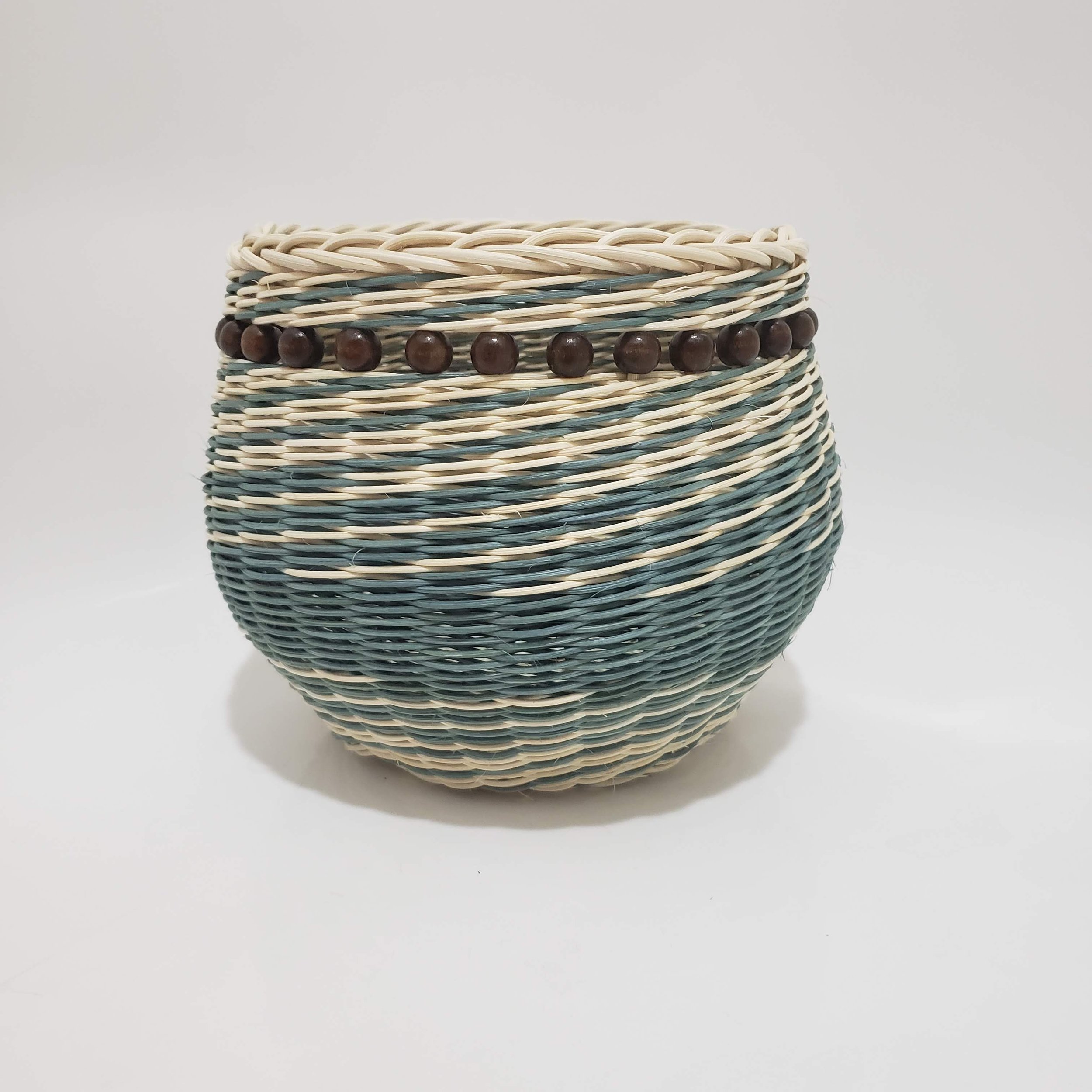A woven basket with a simple pattern of cream, blue, and brown sections, featuring decorative wooden beads on one of the cream-colored areas.