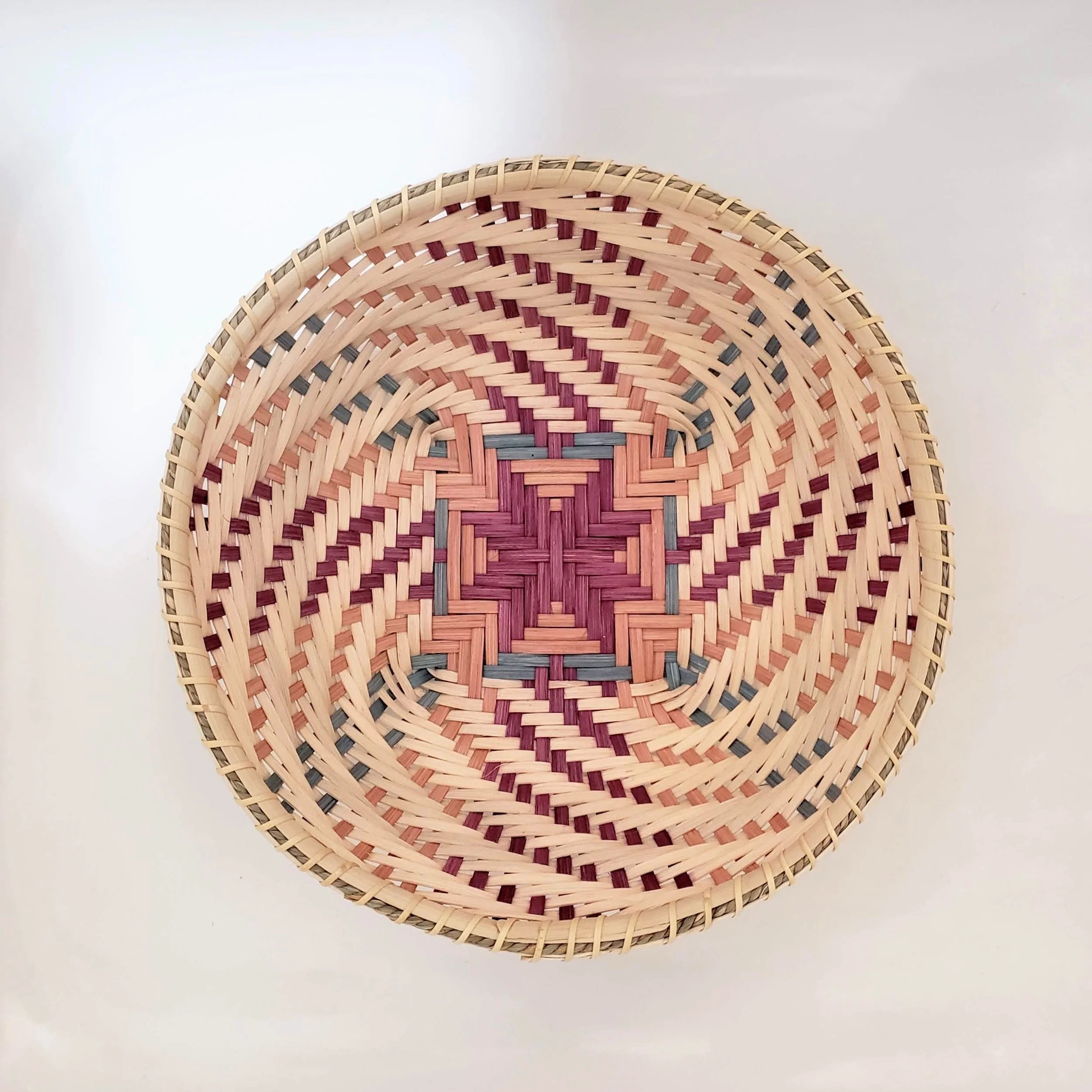 Close-up of a round woven basket with intricate pattern, placed on a white surface.