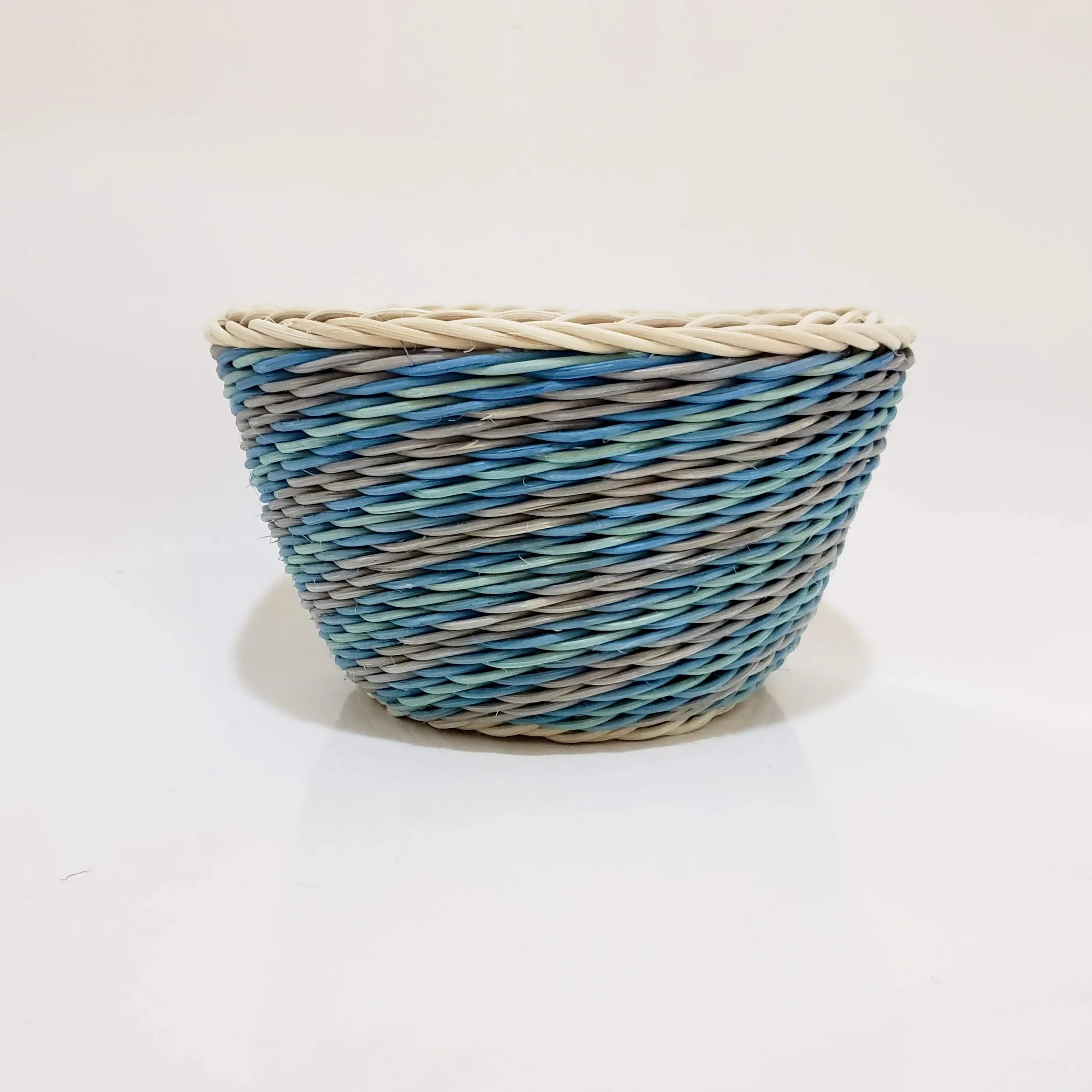 Close-up of a woven basket made of multiple colors of plastic strips, including beige, blue, green, gray, and black, against a plain white background.