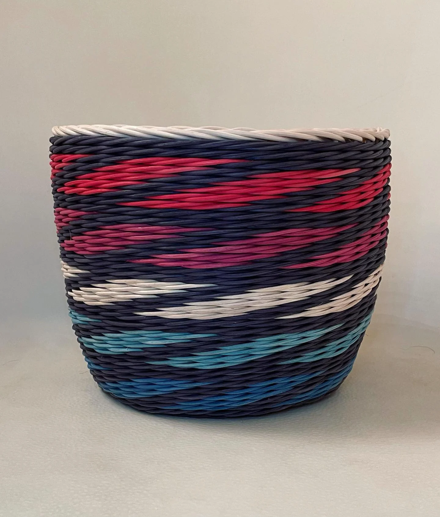 Colorful woven basket with red, blue, black, white, and pink patterns, placed on a plain surface.