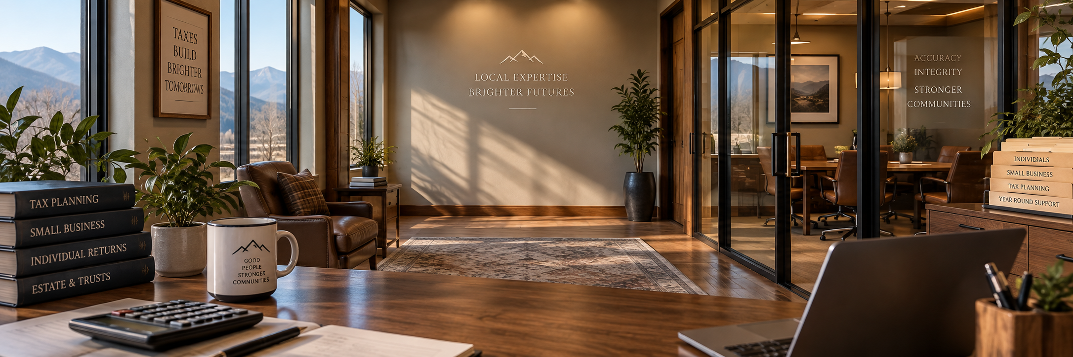 Interior of a modern office with wooden floors and large windows showing mountains outside. There are plants, framed artwork, leather chairs, a desk with books on tax planning and small business, a calculator, a coffee mug, a laptop, and a glass-walled meeting room with more chairs. Walls have motivational phrases about expertise and community.