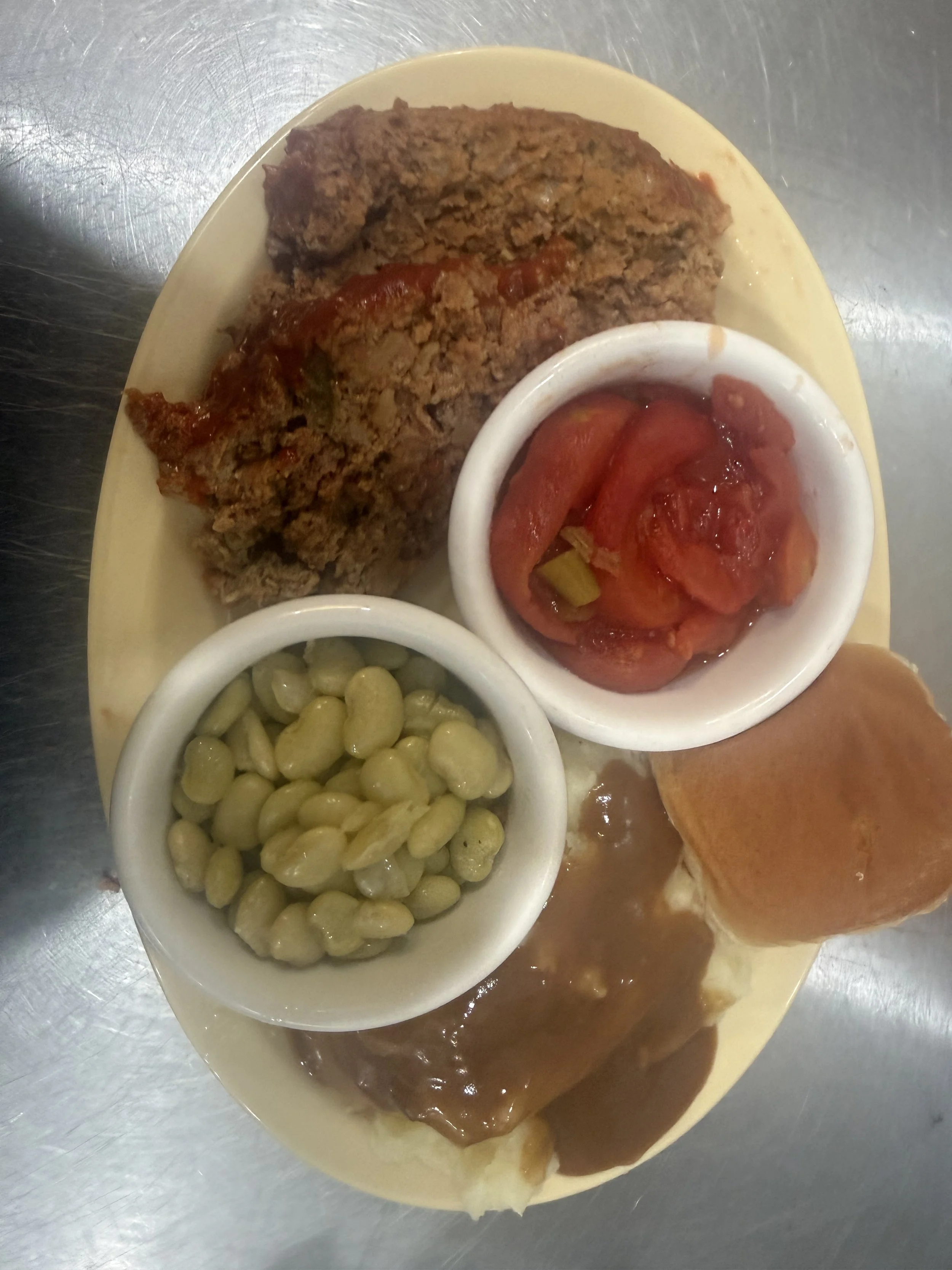 Plate of food including chili with beans, a meatloaf with tomato sauce, green beans, and a bread roll.