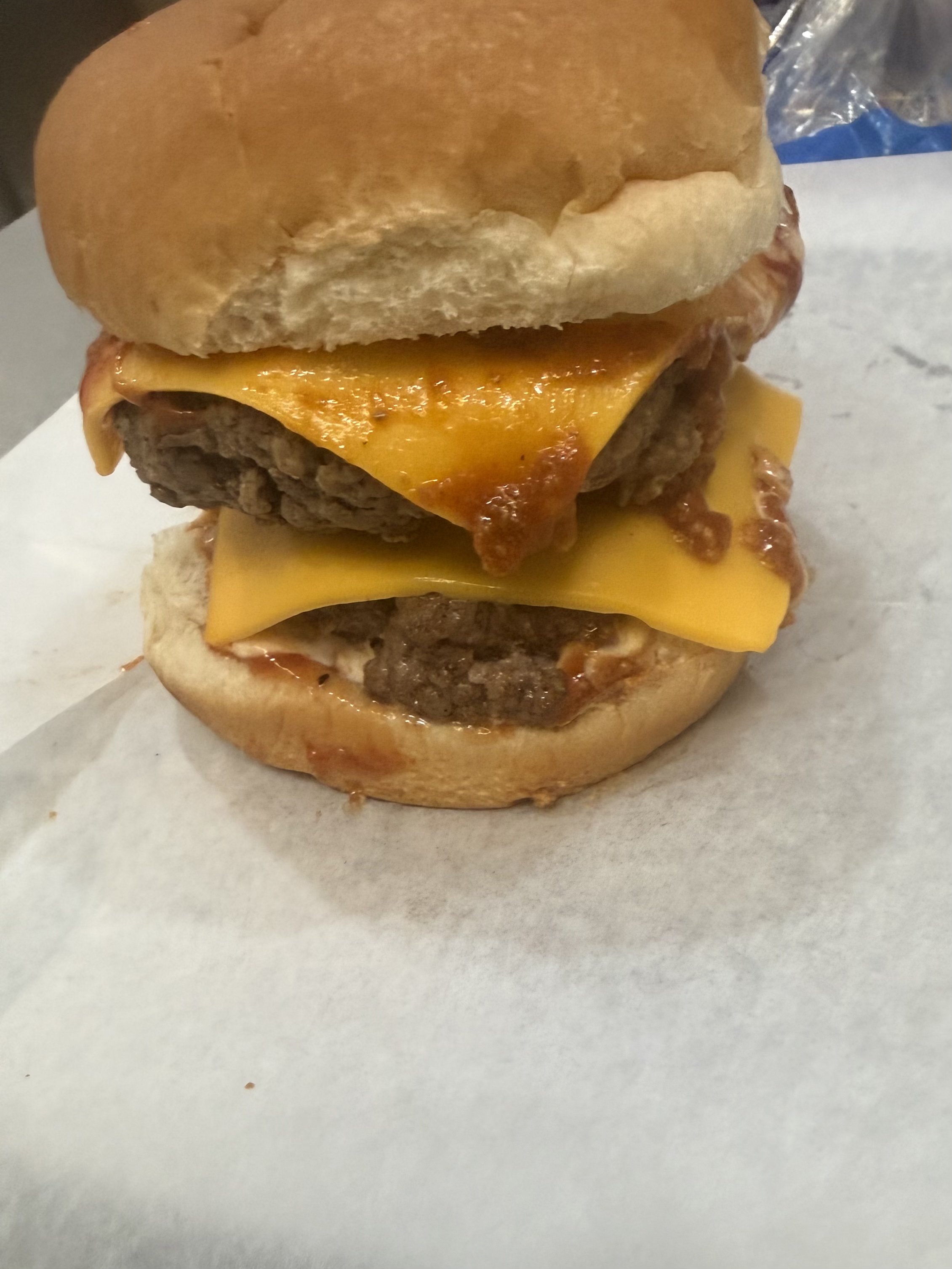 A cheeseburger with a beef patty, melted cheese, and a sandwich bun, placed on white paper.