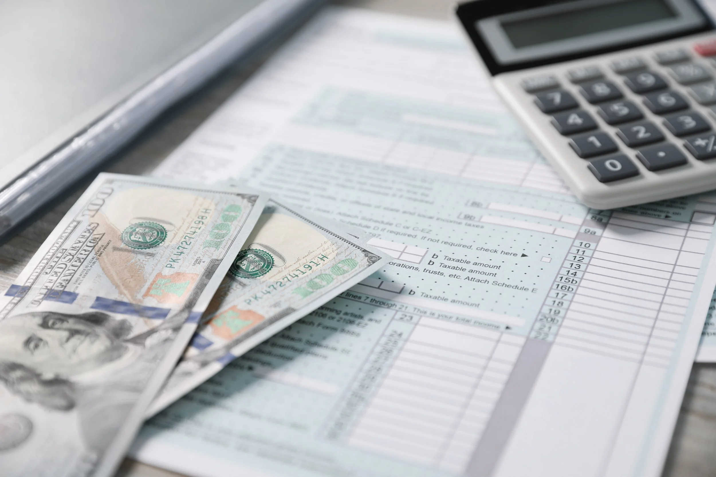 Close-up of a calculator, U.S. dollar bills, and a tax form or financial document on a desk.