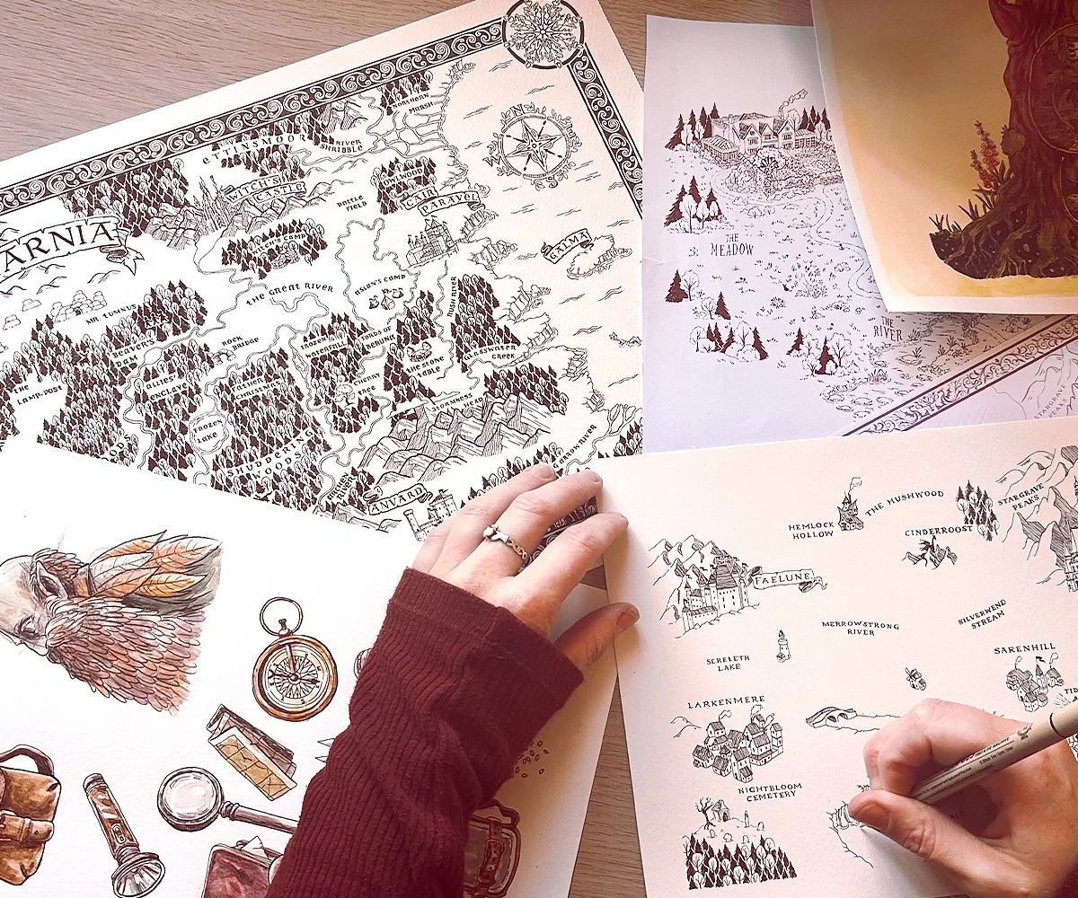 Various detailed illustrated maps and drawings of fantasy or storybook lands on paper, some being sketched or colored by hands, with forested areas, castles, rivers, and labeled locations.