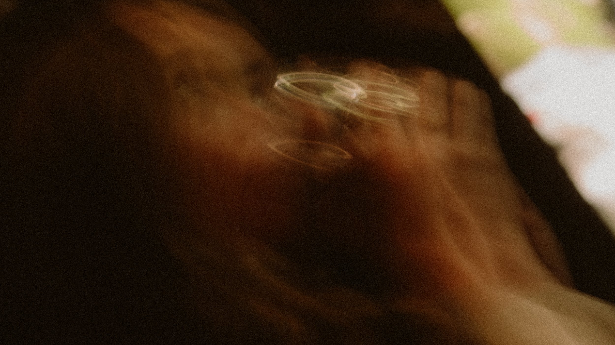 Blurry close-up of a person's face with glasses, with warm lighting creating a bokeh effect.