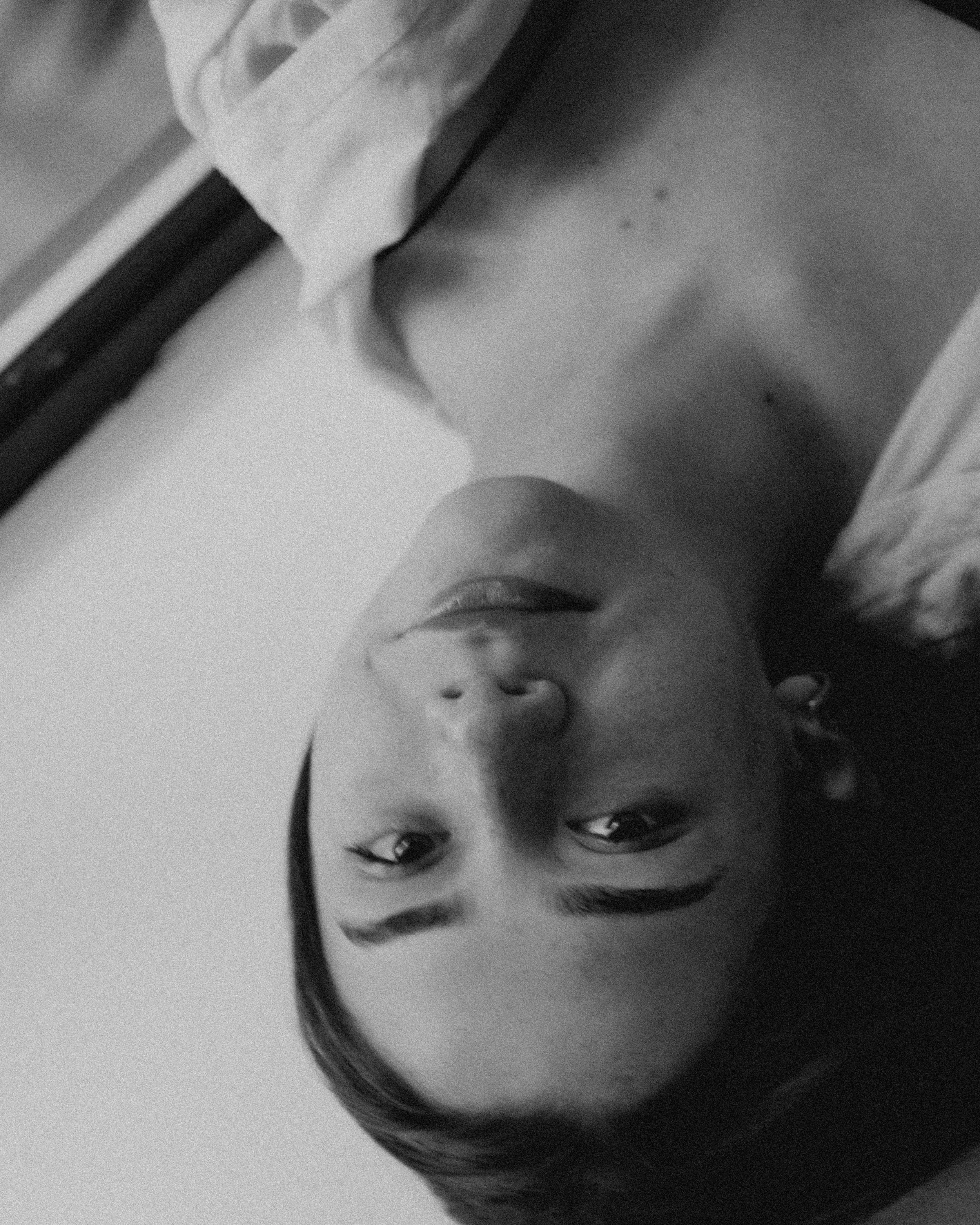 Close-up black and white photo of a person's face, inverted in orientation, showing eyes, nose, and lips.
