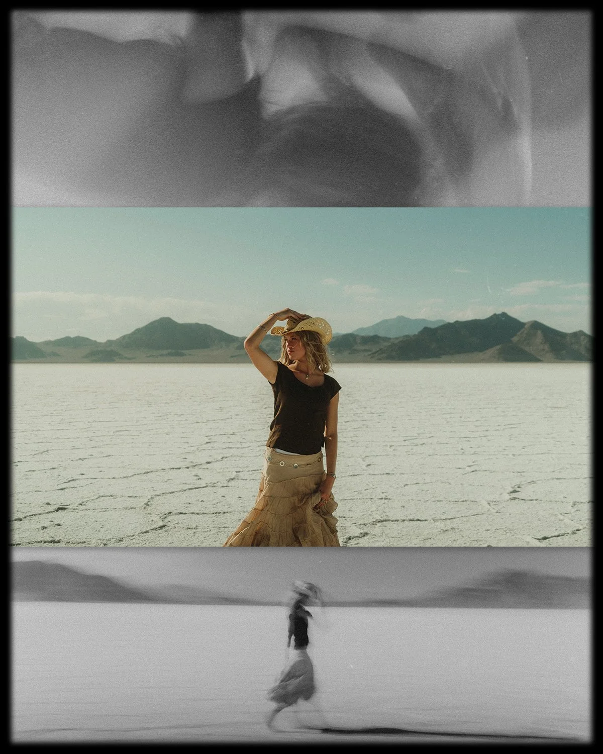 A woman in a black top and beige skirt standing in a desert landscape with mountains in the background, holding a straw hat on her head.