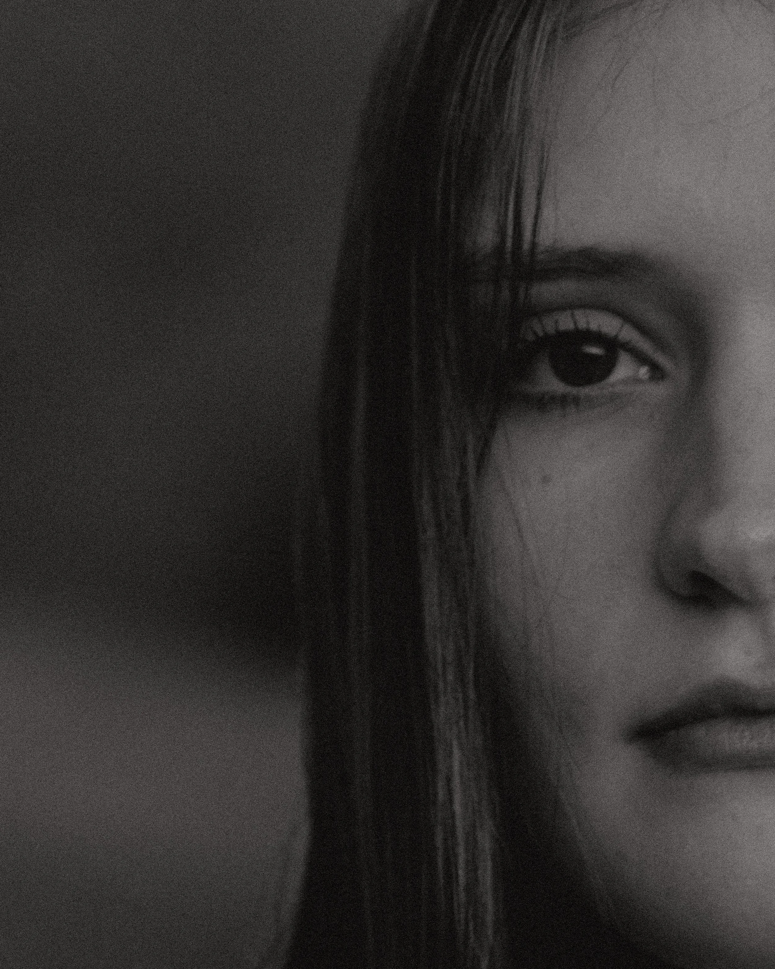 Close-up of a person's eye and part of their face, with hair partially covering the eye, black and white photo.