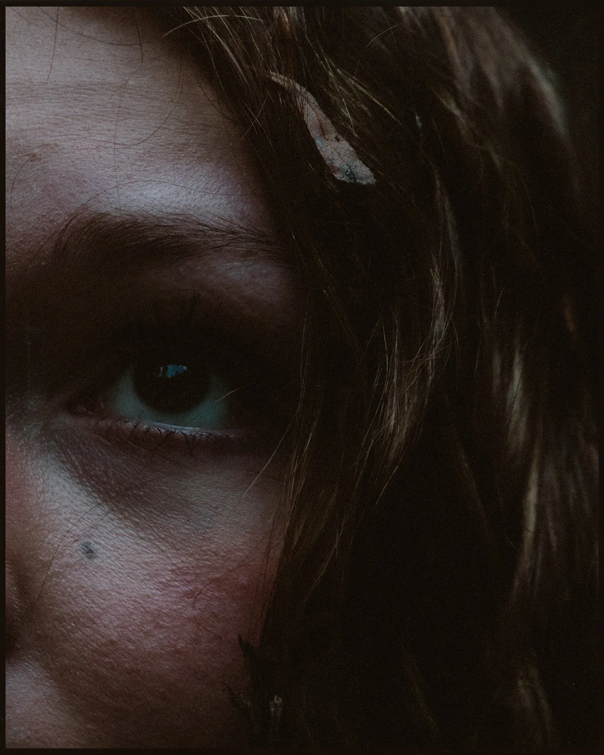 Close-up of a person's face showing their eye, eyebrow, makeup, and dark hair.