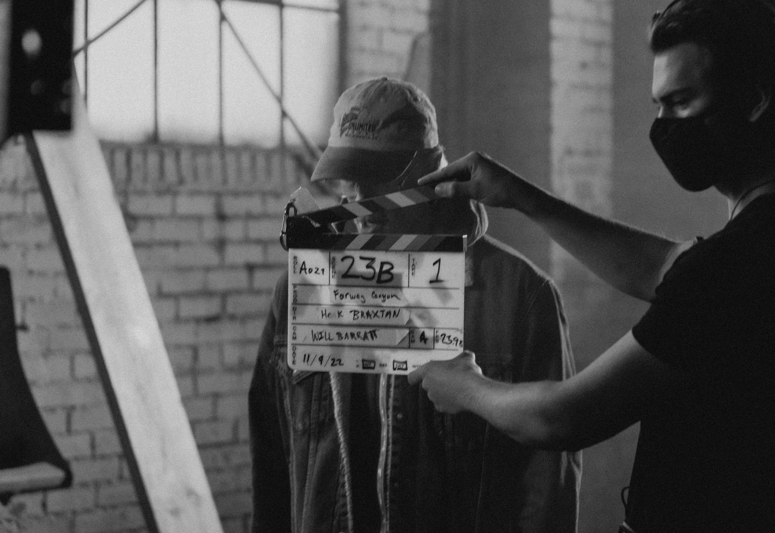 A person holding a film clapperboard labeled "Forbes Canyon" and "He K. Braxtan" during a film shoot with a brick wall in the background.