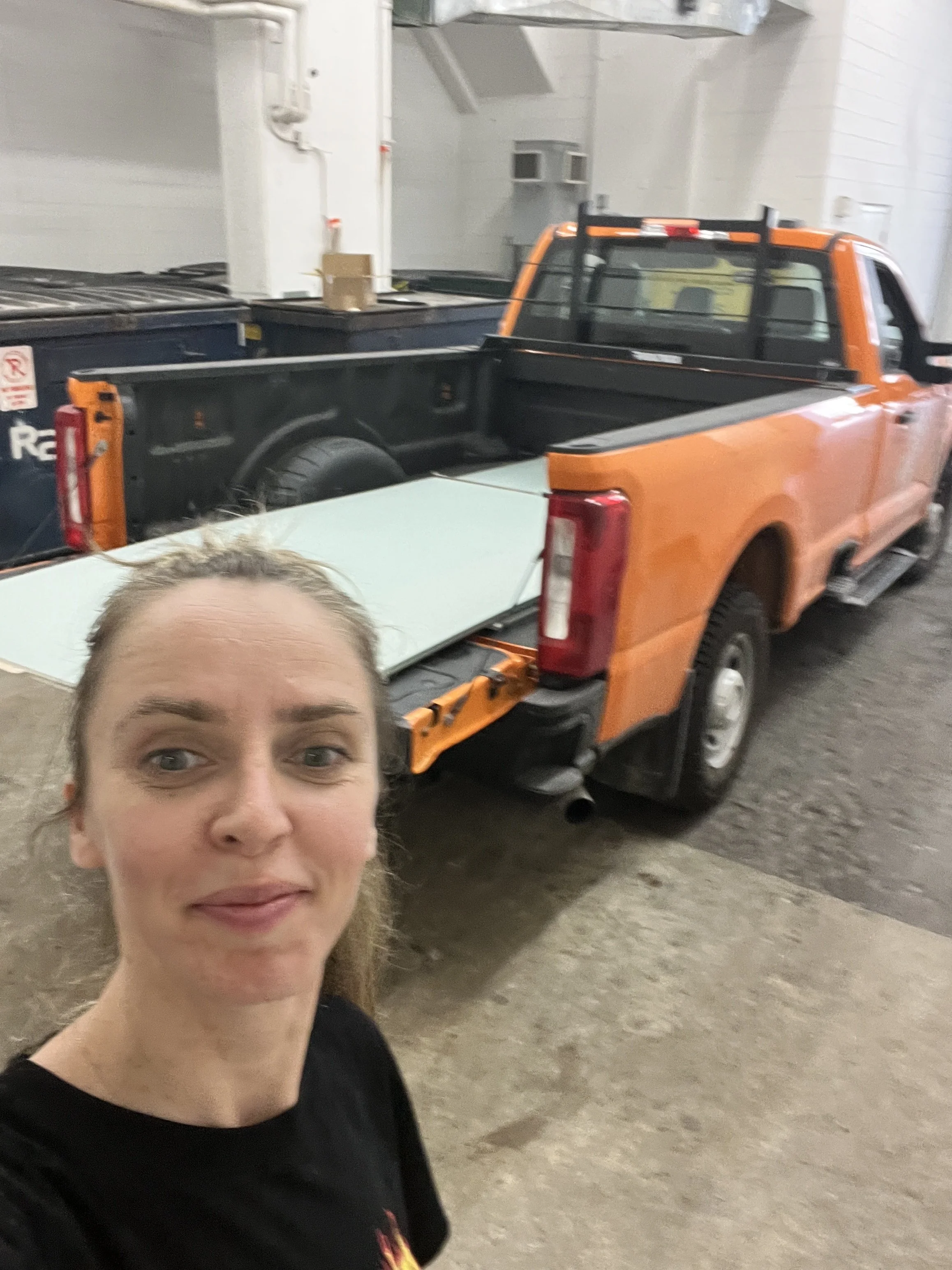 Valentina, owner of Vogman Design + Build, in front of an orange pickup truck loaded with drywall for delivery to a job site