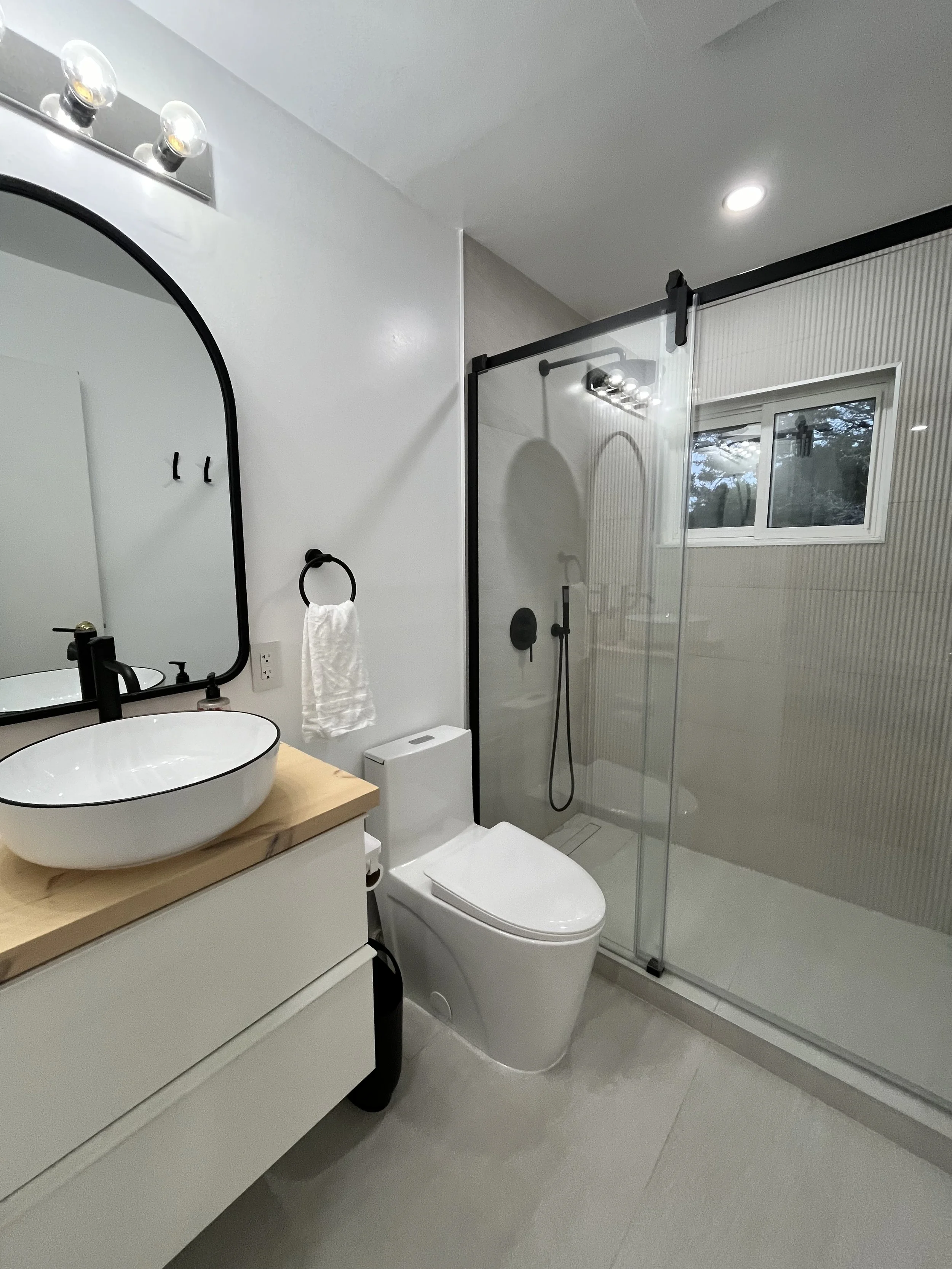Full view of a bathroom in the Tobermory cottage renovation with a black-framed glass shower, floating vessel sink vanity, arched mirror, and modern toilet