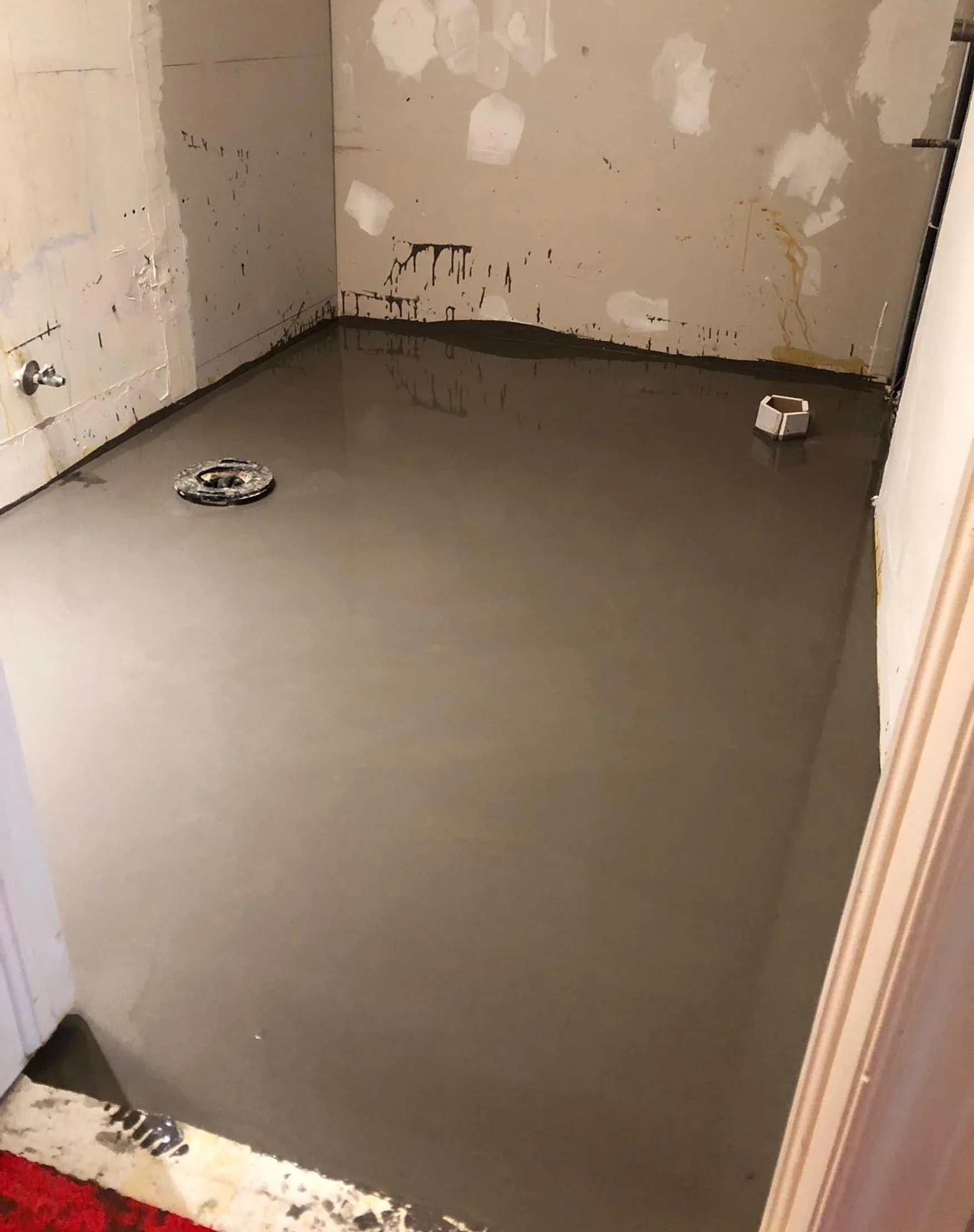 Freshly poured self-leveling underlayment covering the bathroom floor around the drain, during the Queen West condo bathroom renovation