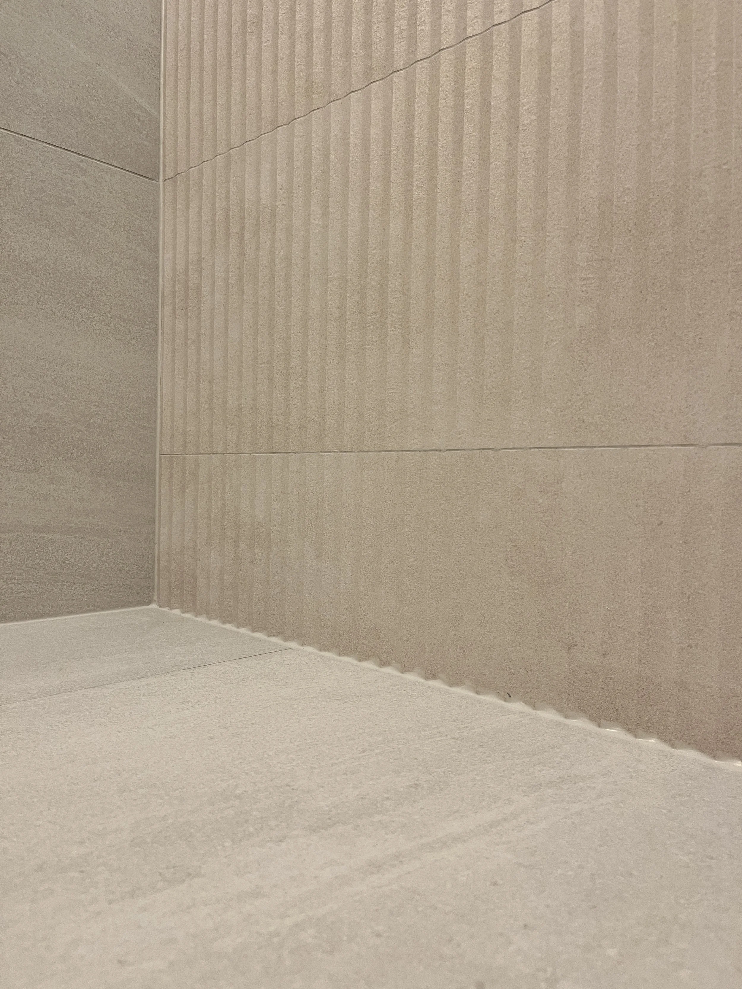 Close-up of a mitred corner where fluted accent tile meets flat stone-look tile in a Queen West condo bathroom renovation