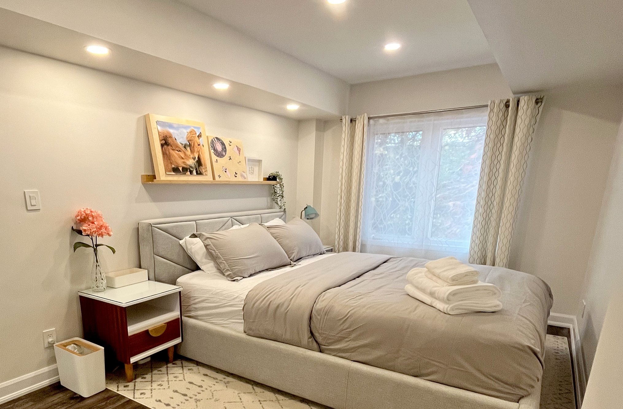 After photo of THE OASIS bedroom renovation with a grey upholstered bed, wood floating shelf styled with framed horse art, and a mid-century nightstand